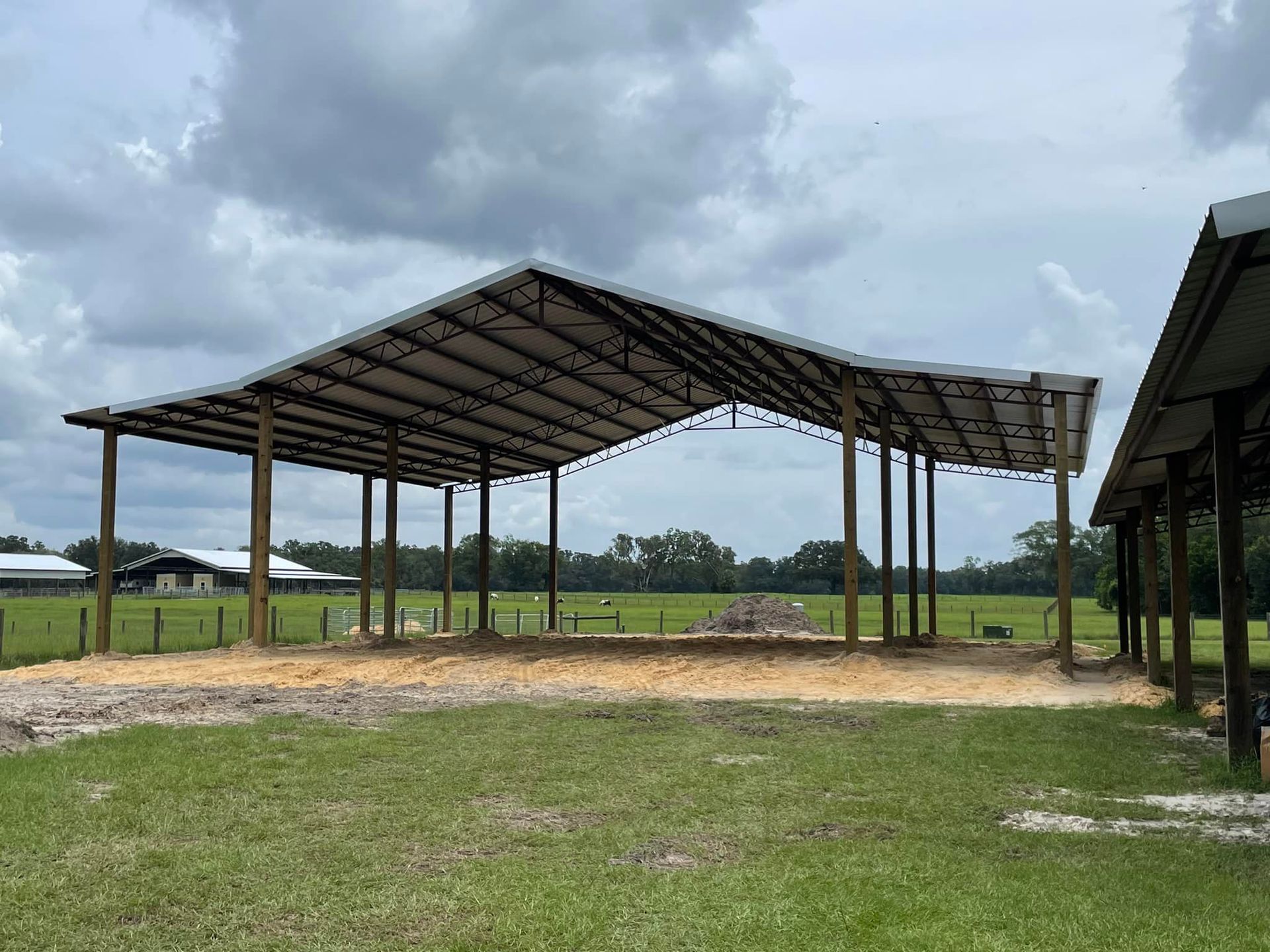 A large metal building is being built in the middle of a grassy field.