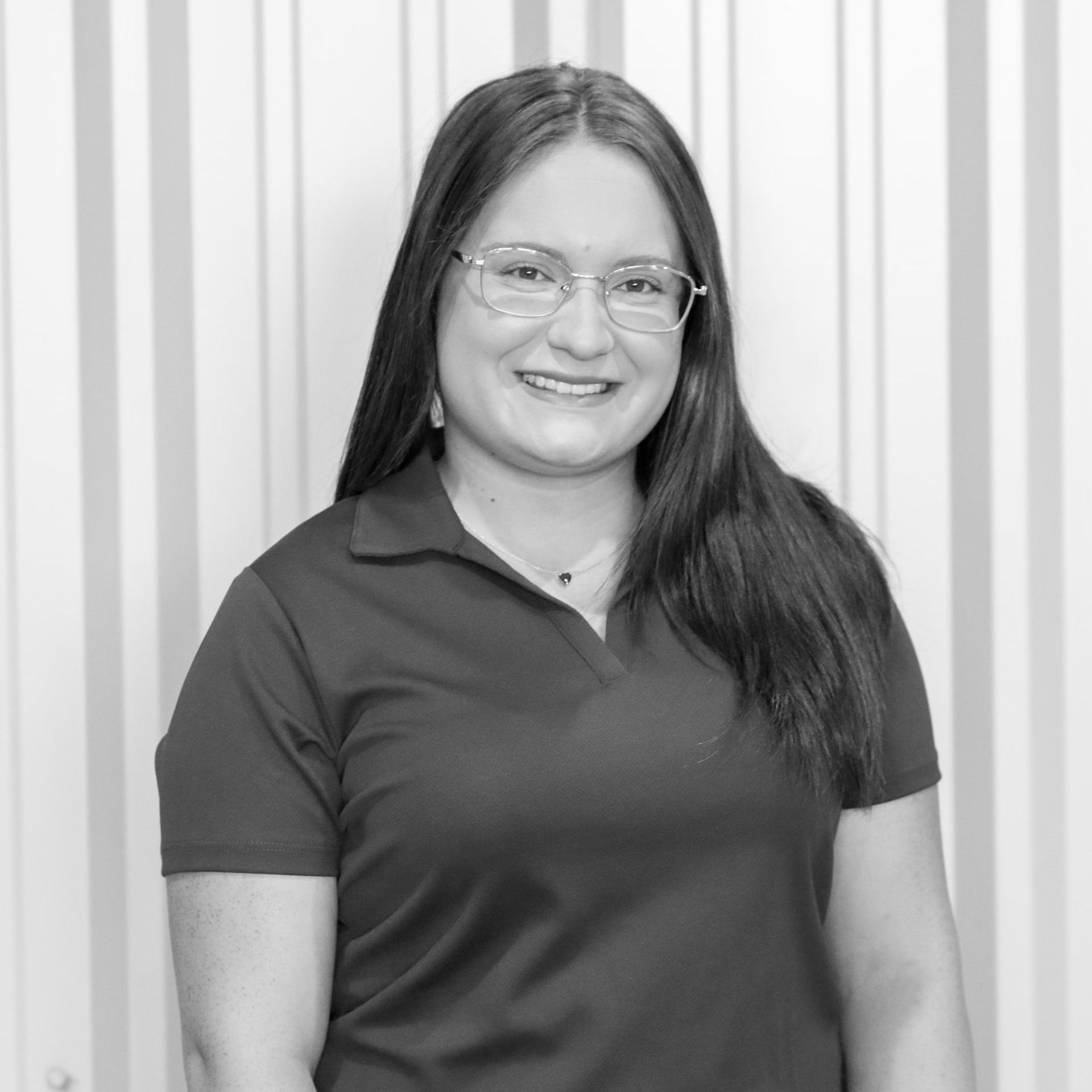 A woman wearing glasses and a black shirt is smiling in a black and white photo.