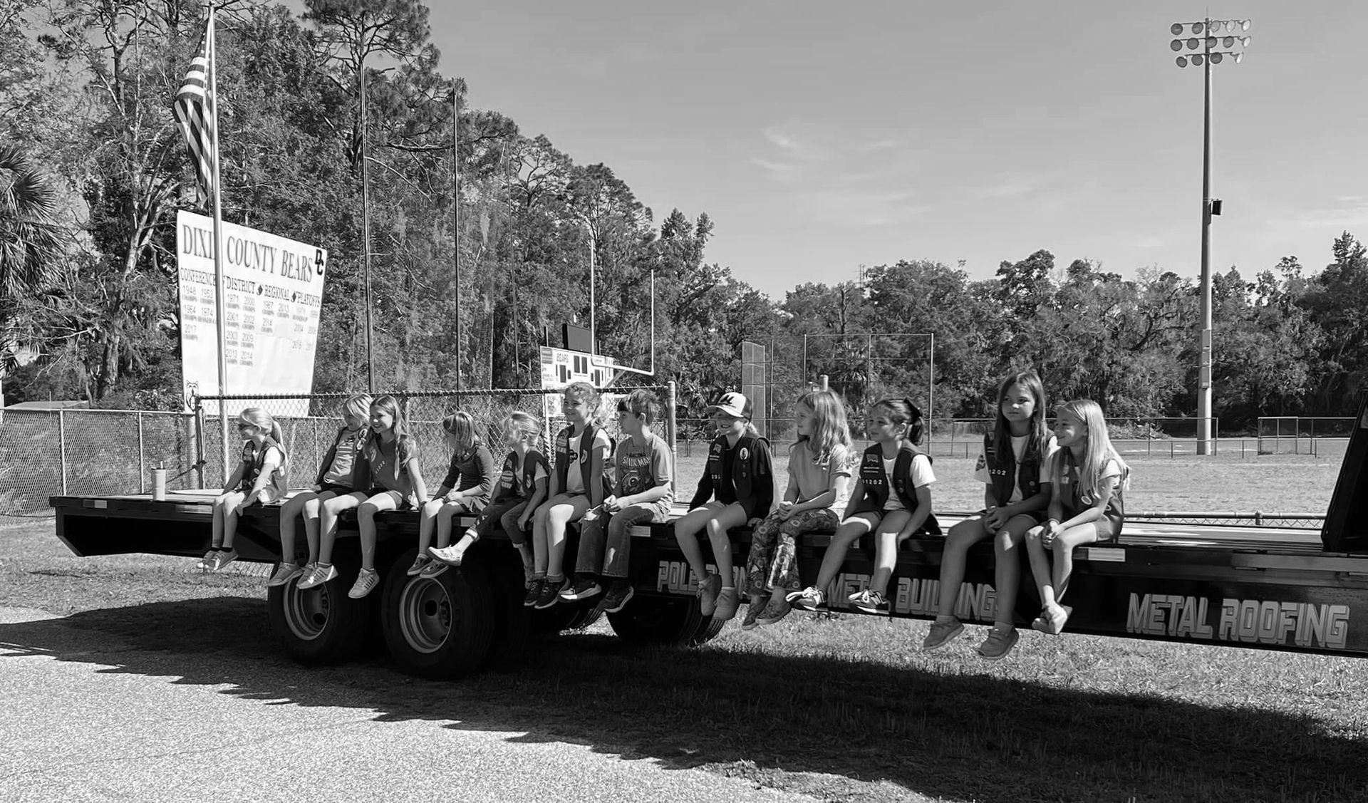 A black and white photo of a group of people sitting on a trailer.