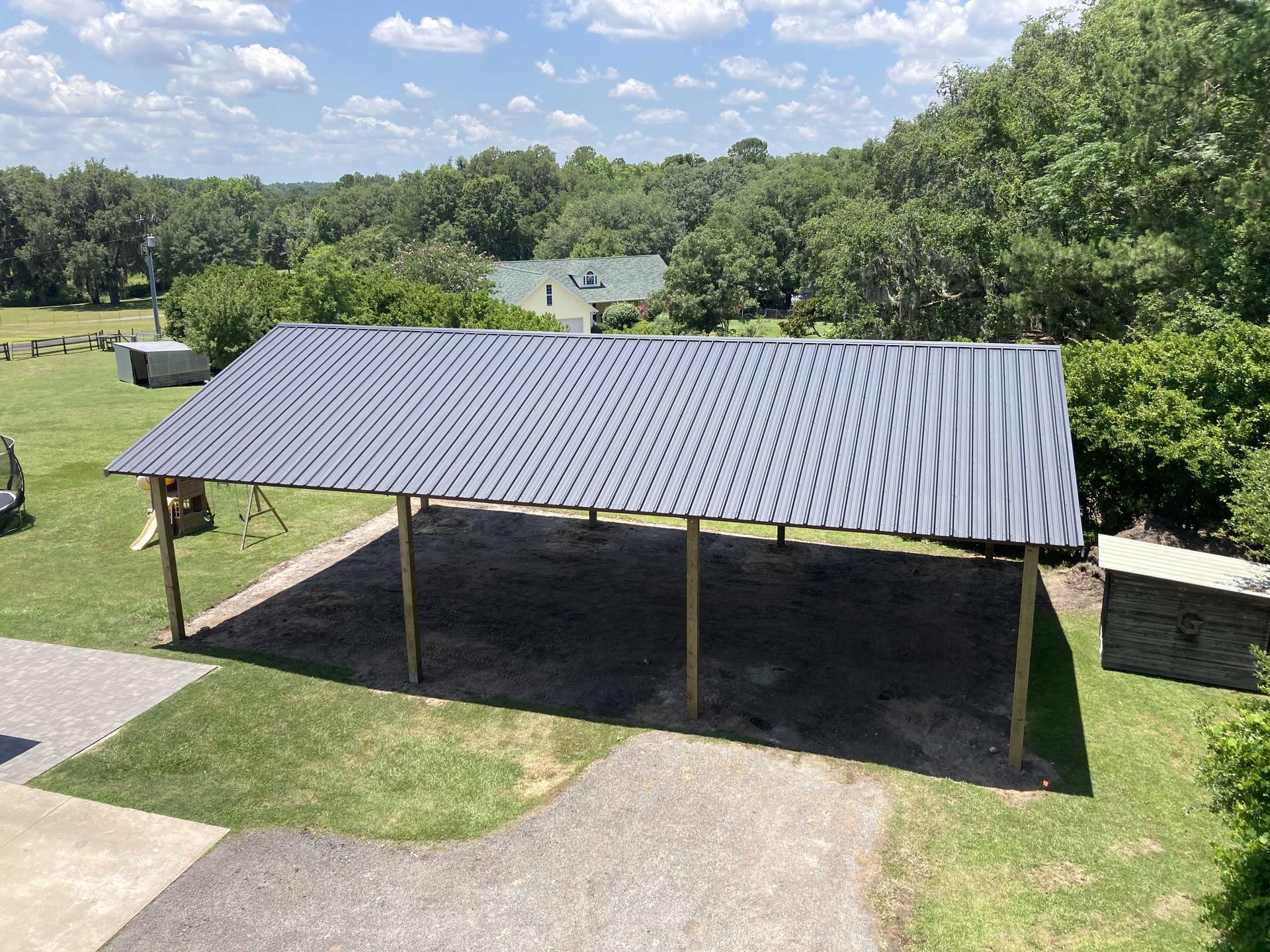 An aerial view of a pole barn with a black roof surrounded by trees.