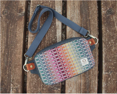 Colorful woven crossbody bag with blue strap on a rustic wooden surface