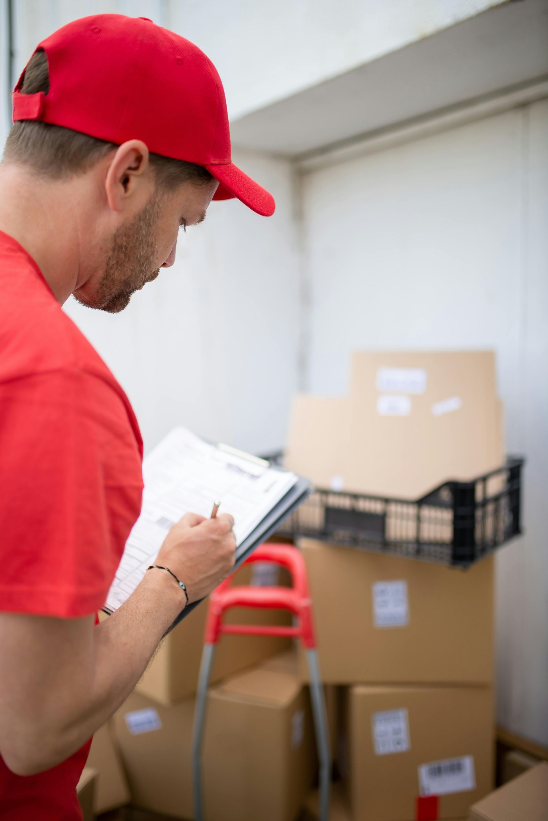 A delivery man is writing on a clipboard in front of a stack of boxes.