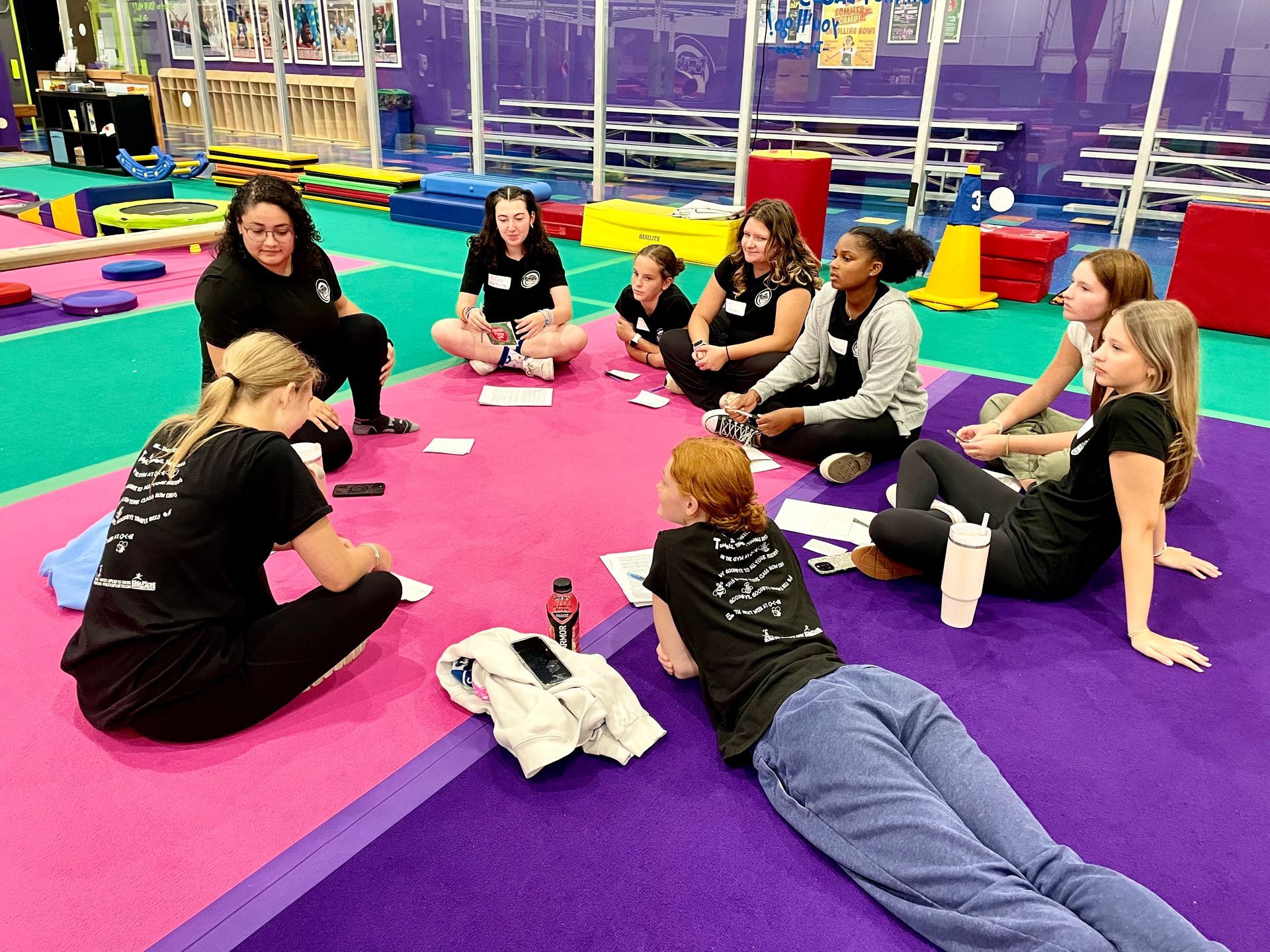 Group sitting in a colorful indoor play area, gathered in a circle on mats for an activity.