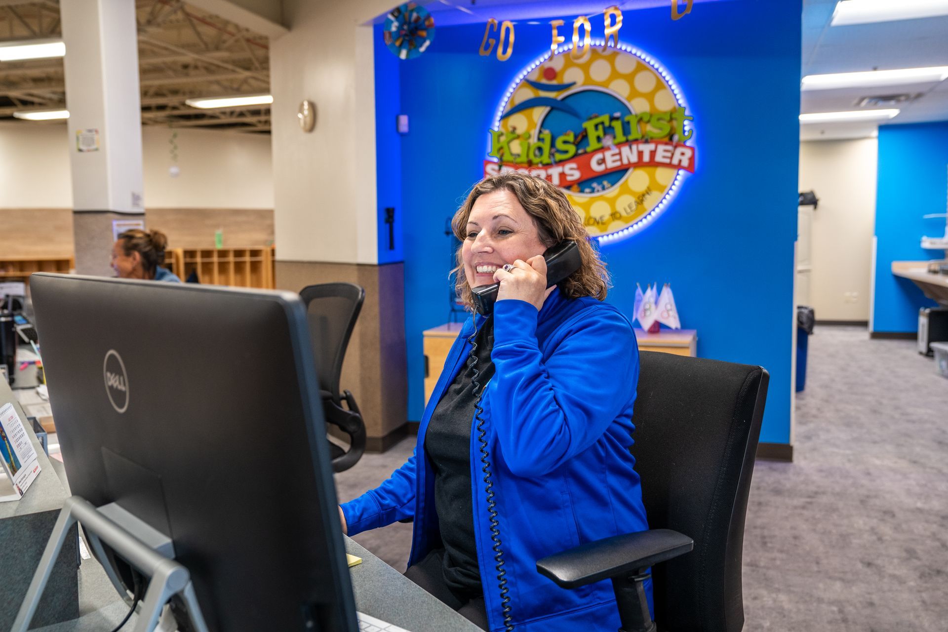 A woman is sitting at a desk in front of a computer talking on a phone.