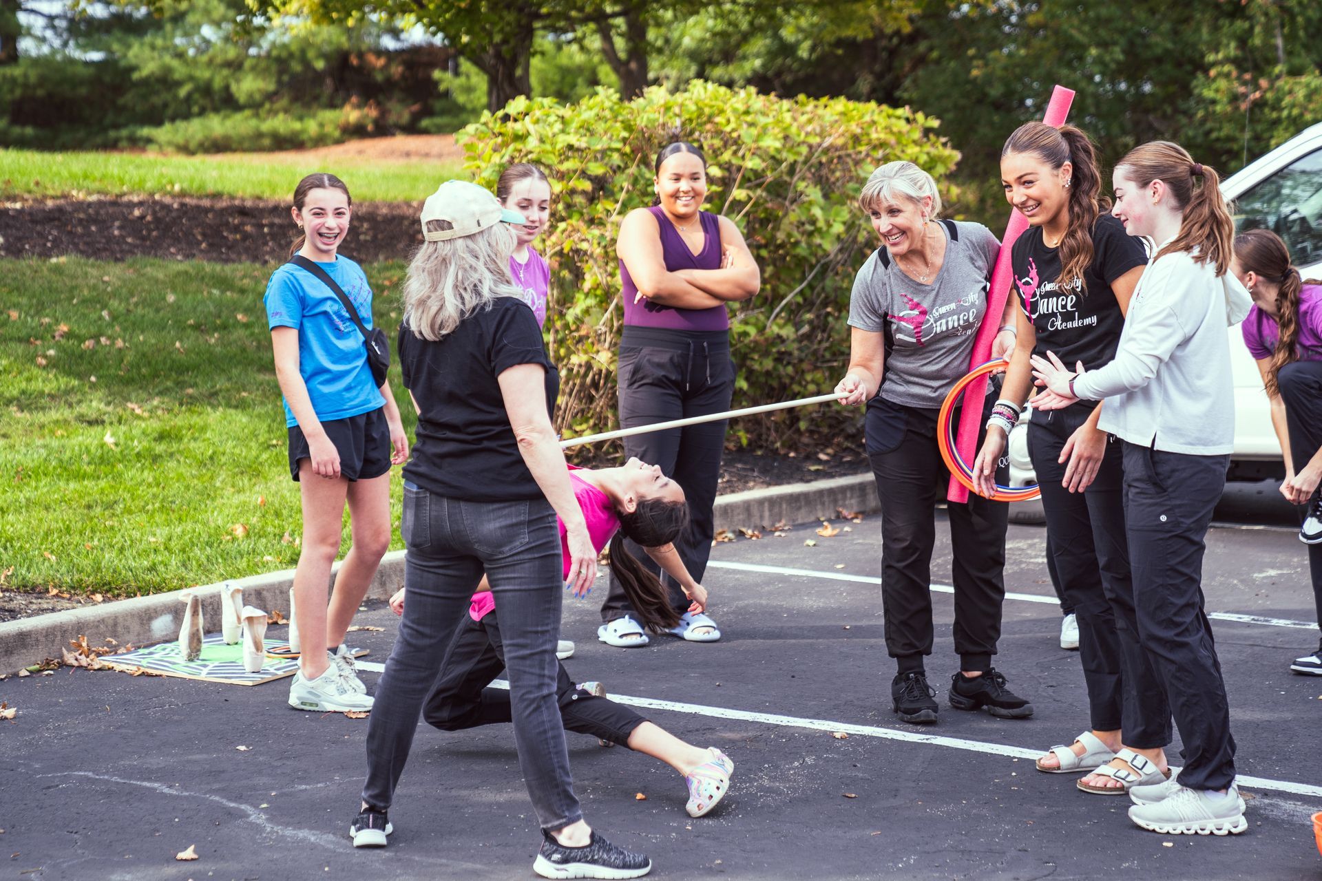People playing limbo outdoors on a paved path, with others watching nearby.