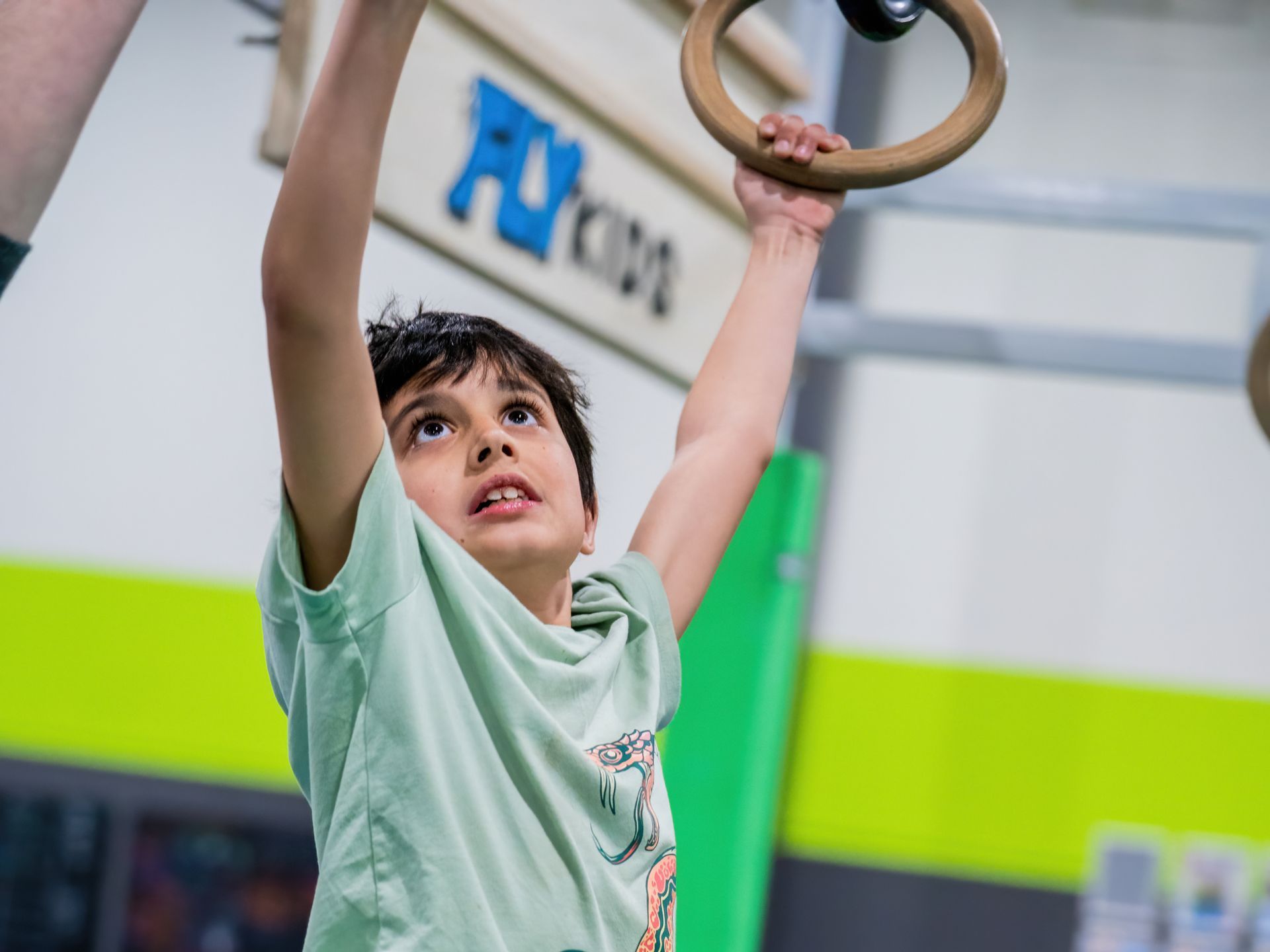 Child reaching up to grab gym rings in a bright indoor play area.