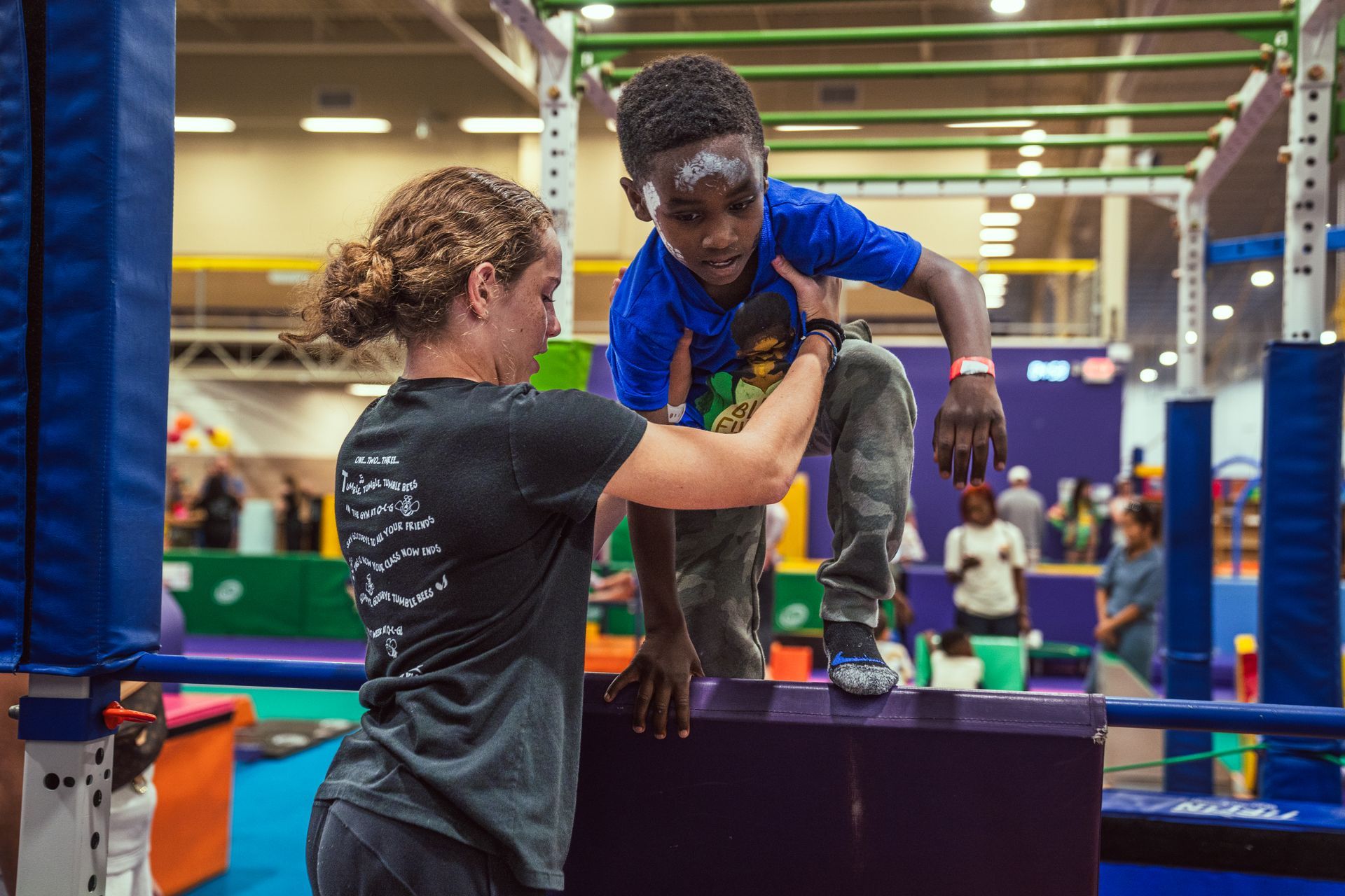 Child climbing a padded obstacle with an adult spotting them in an indoor play gym