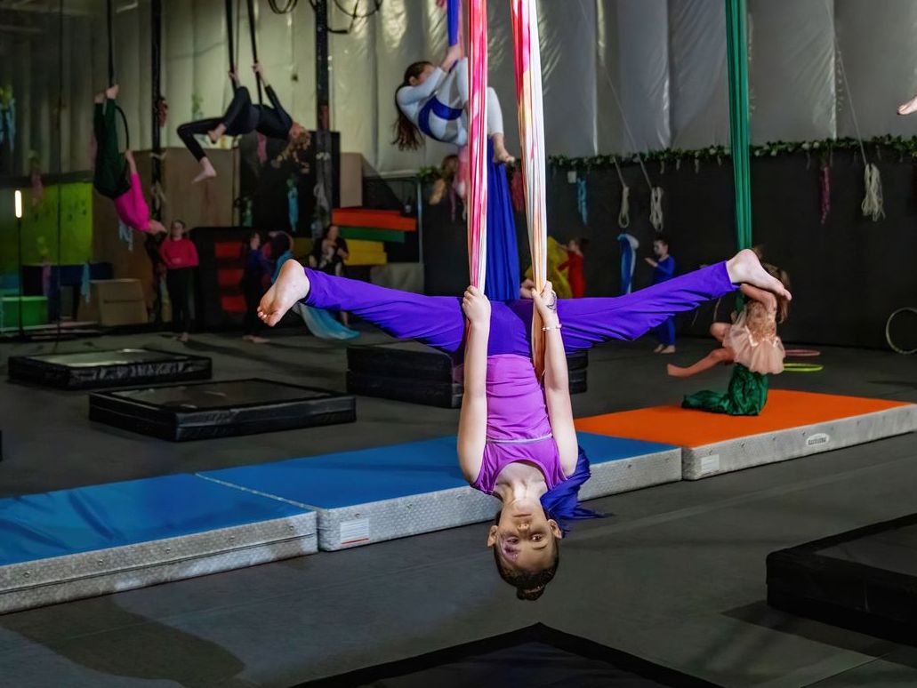 Person hanging upside down in a purple aerial silk class on colorful mats in a studio