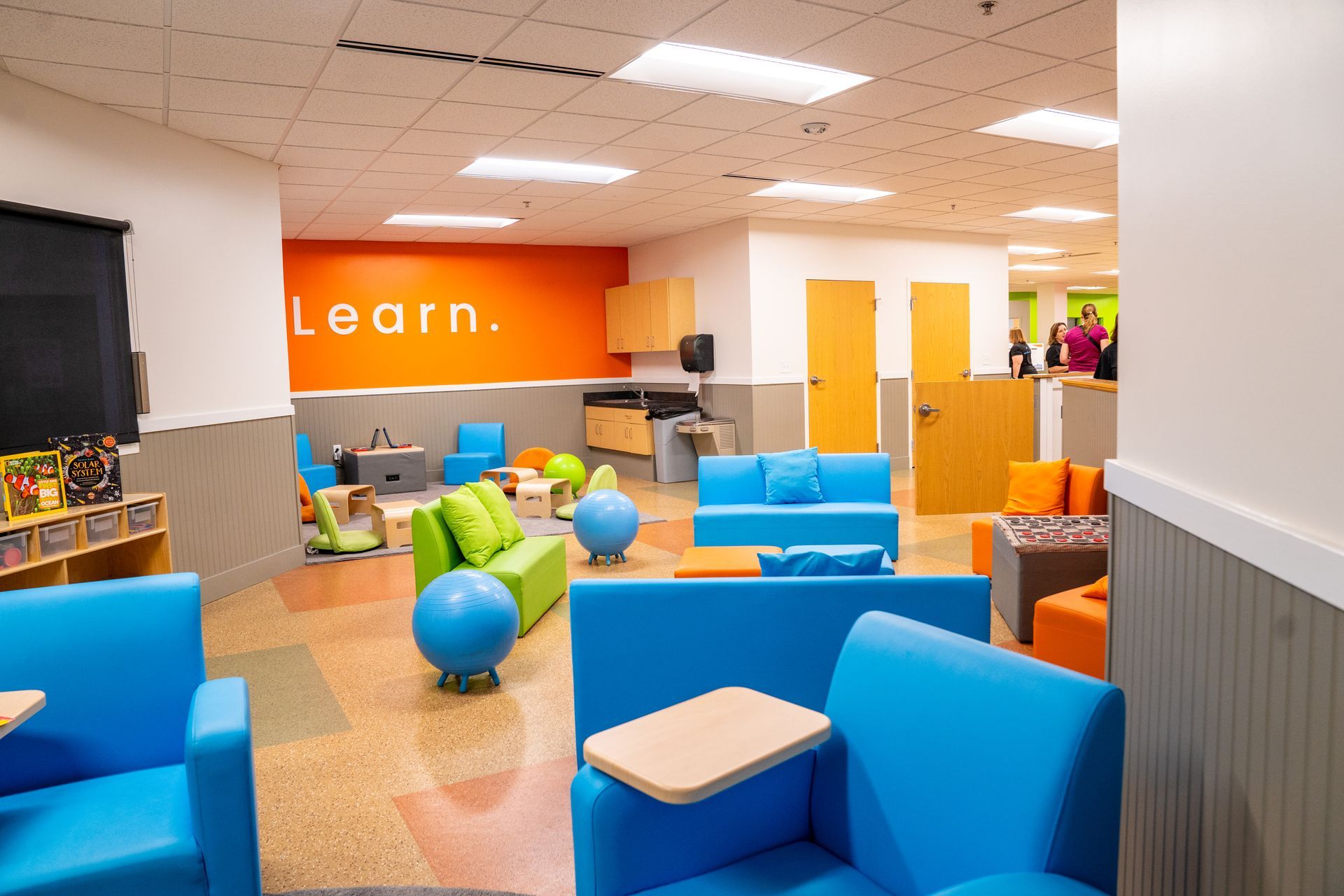A colorful learning space with blue couches and chairs, an orange accent wall with 