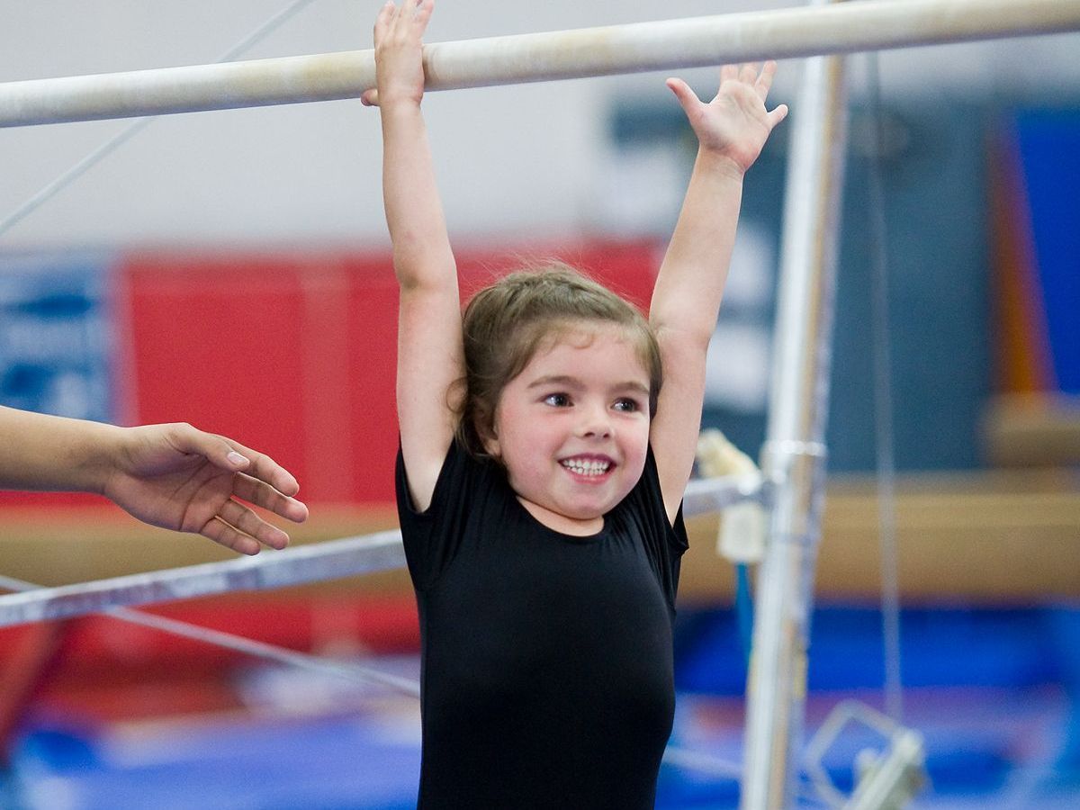 Child smiling while hanging from gymnastics bars in a gym