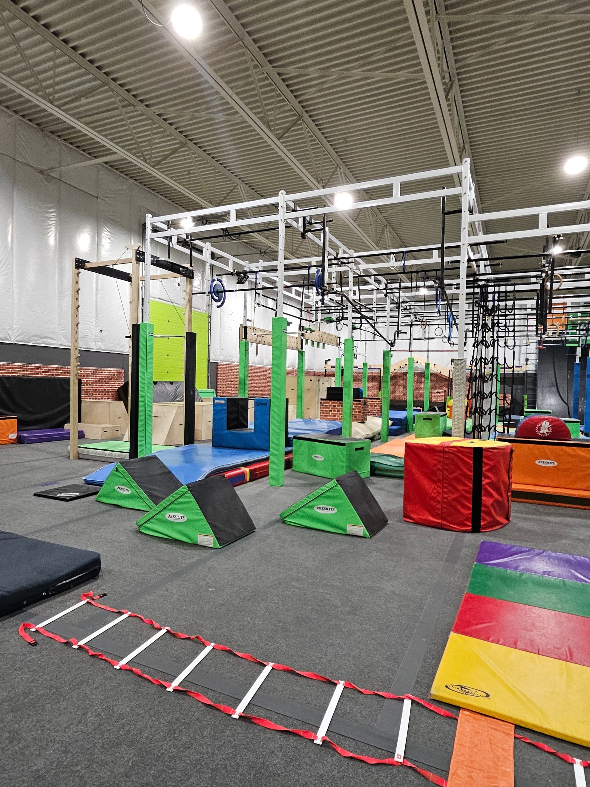 Indoor obstacle course with various green, blue, and red equipment, including a ladder, blocks, and a climbing structure.