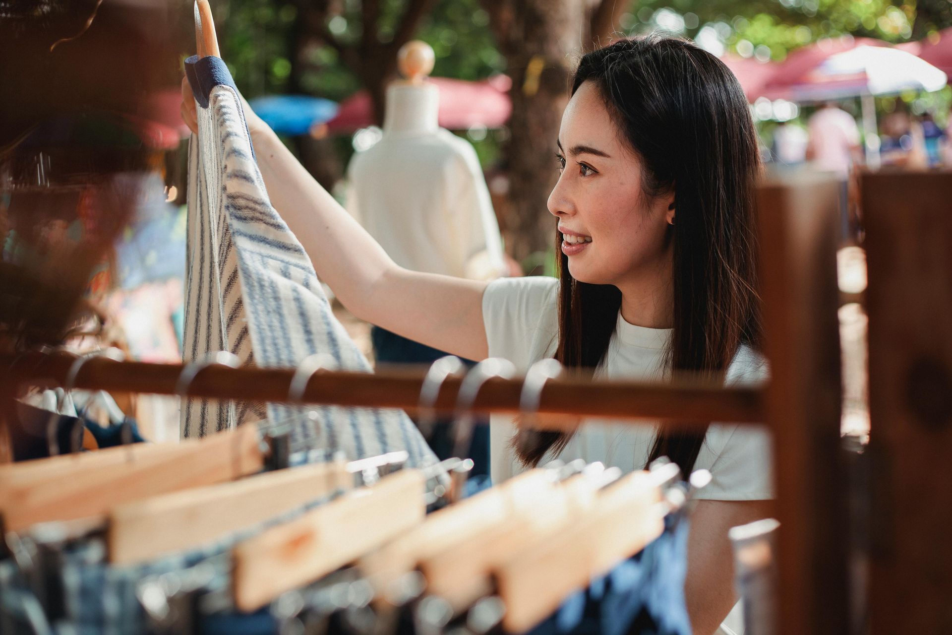 Woman smiling while browsing clothes on a rack in a bright market or boutique