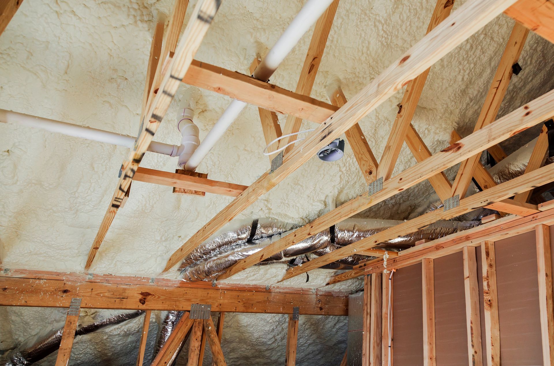 Attic roof framing with exposed wooden trusses and insulation under construction