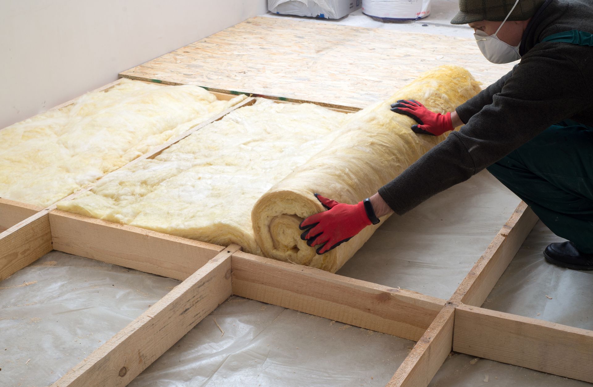 Worker installing yellow insulation in a wooden floor frame