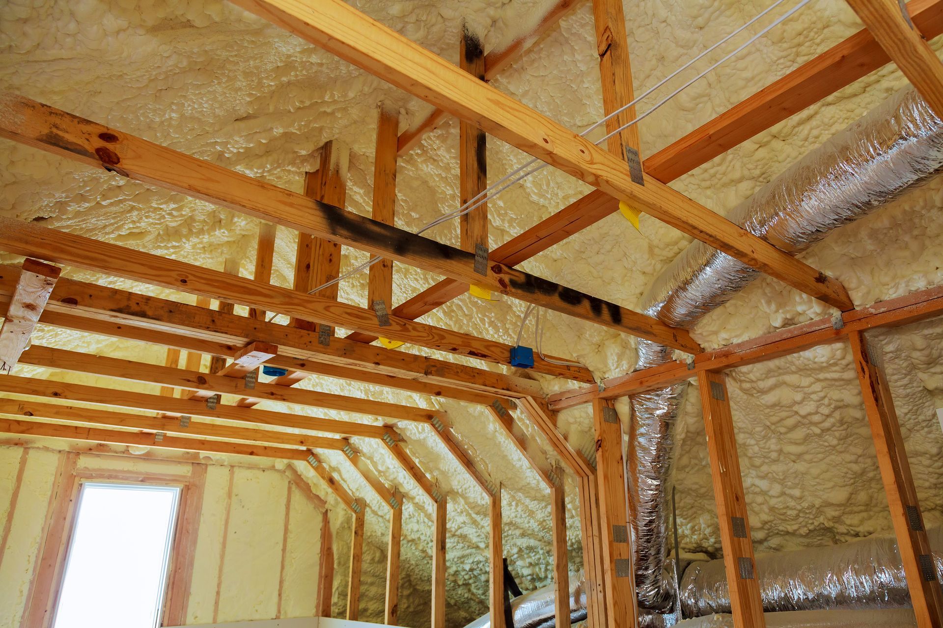 Insulated attic interior with exposed wooden rafters and framing, lit by a small window