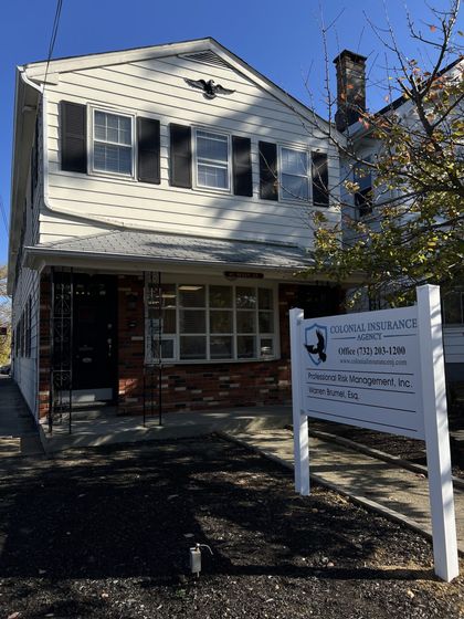 Two-story white house with a brick porch and a sign in front on a sunny day
