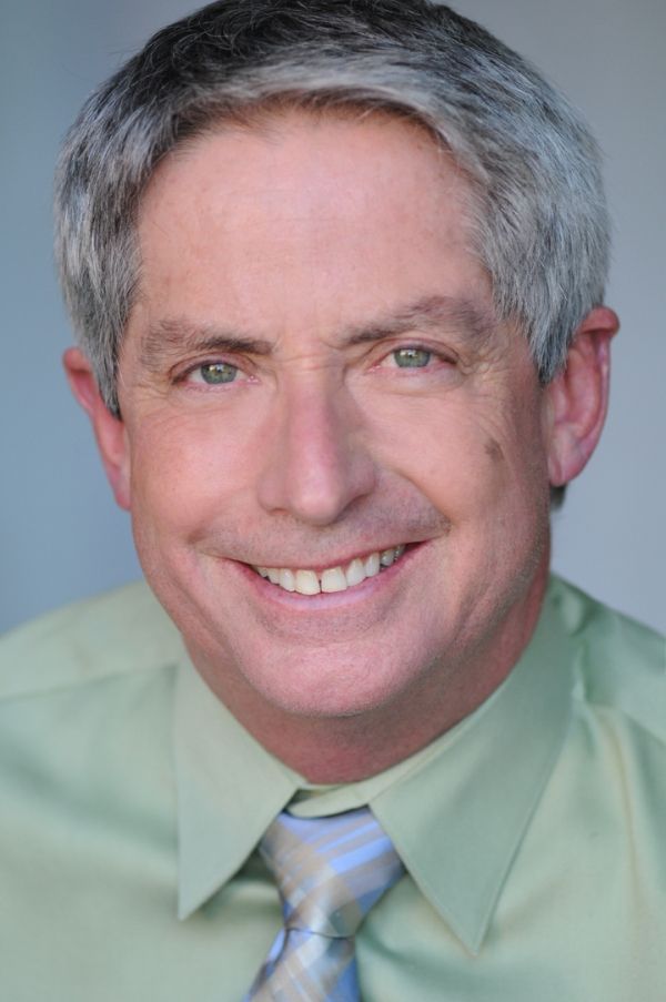 A man in a green shirt and tie is smiling for the camera.