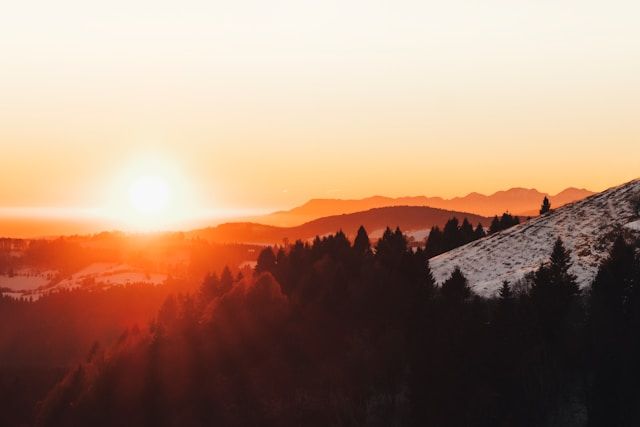 Warm sunset over mountain landscape with glowing sky and silhouetted trees, cremation services Largo, FL