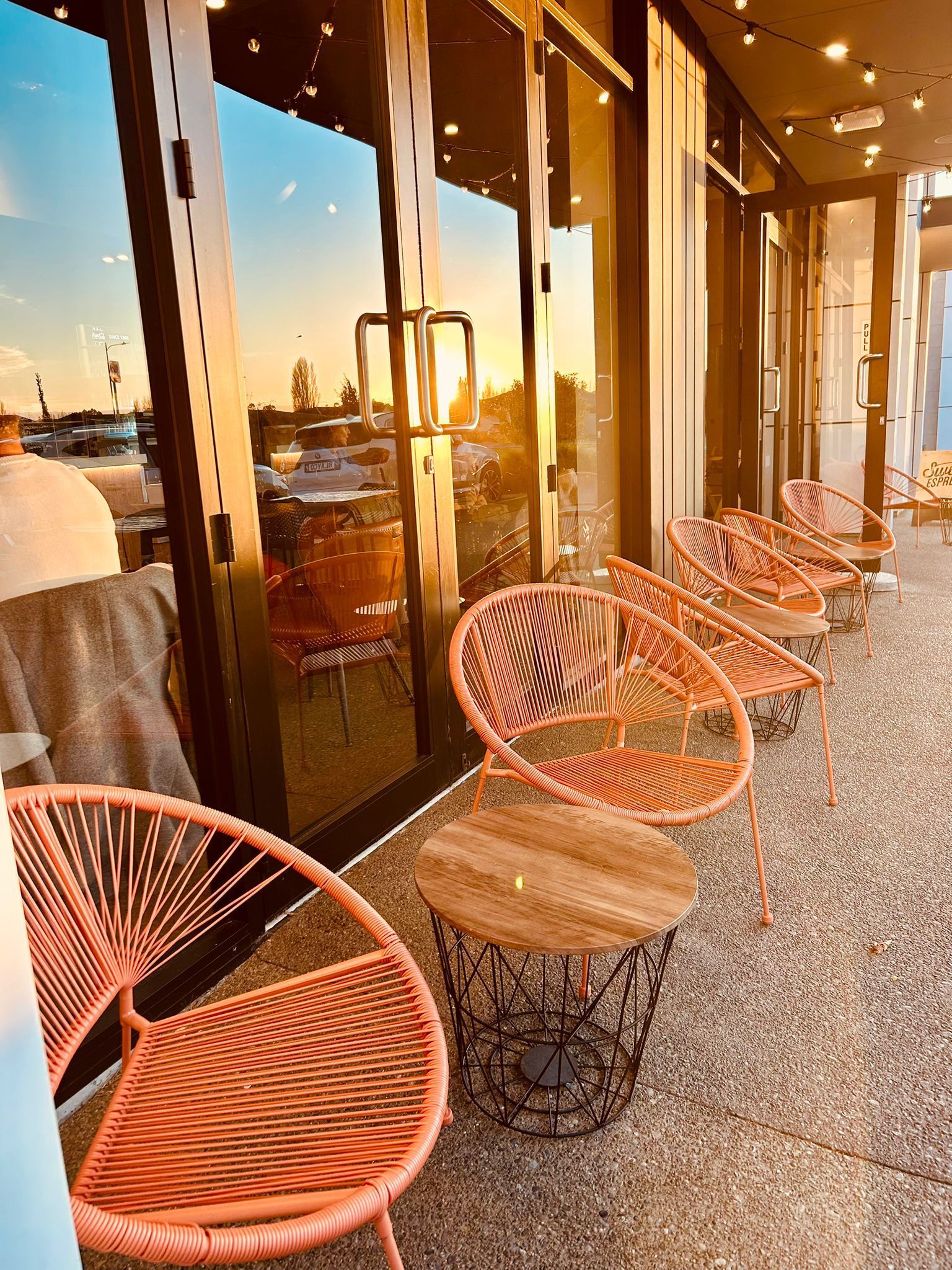 A row of peach-colored wicker patio chairs with small matching tables on a gravel surface at sunset.
