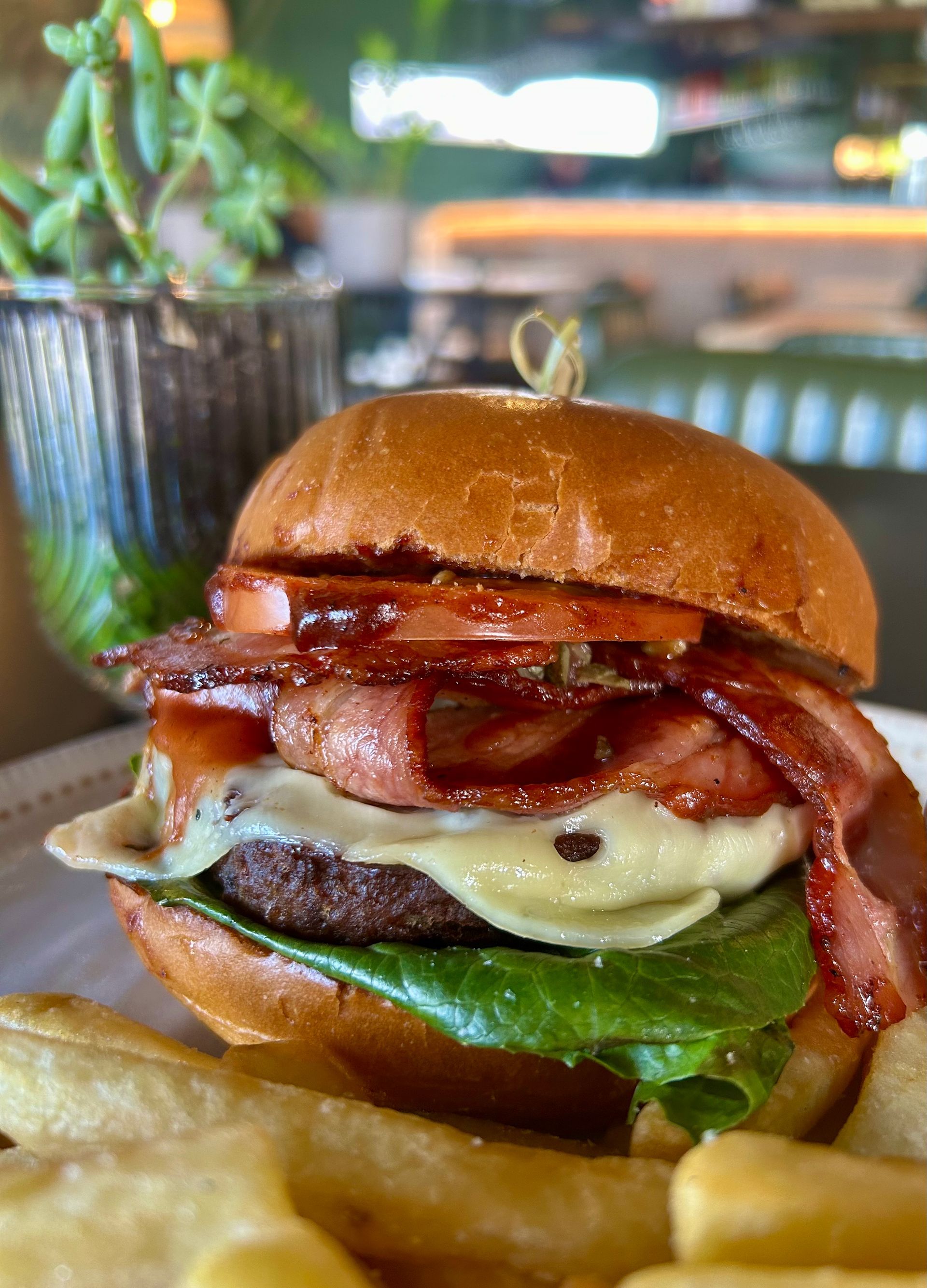 A cheeseburger topped with bacon, lettuce, and tomato, served with a side of fries at a restaurant table.