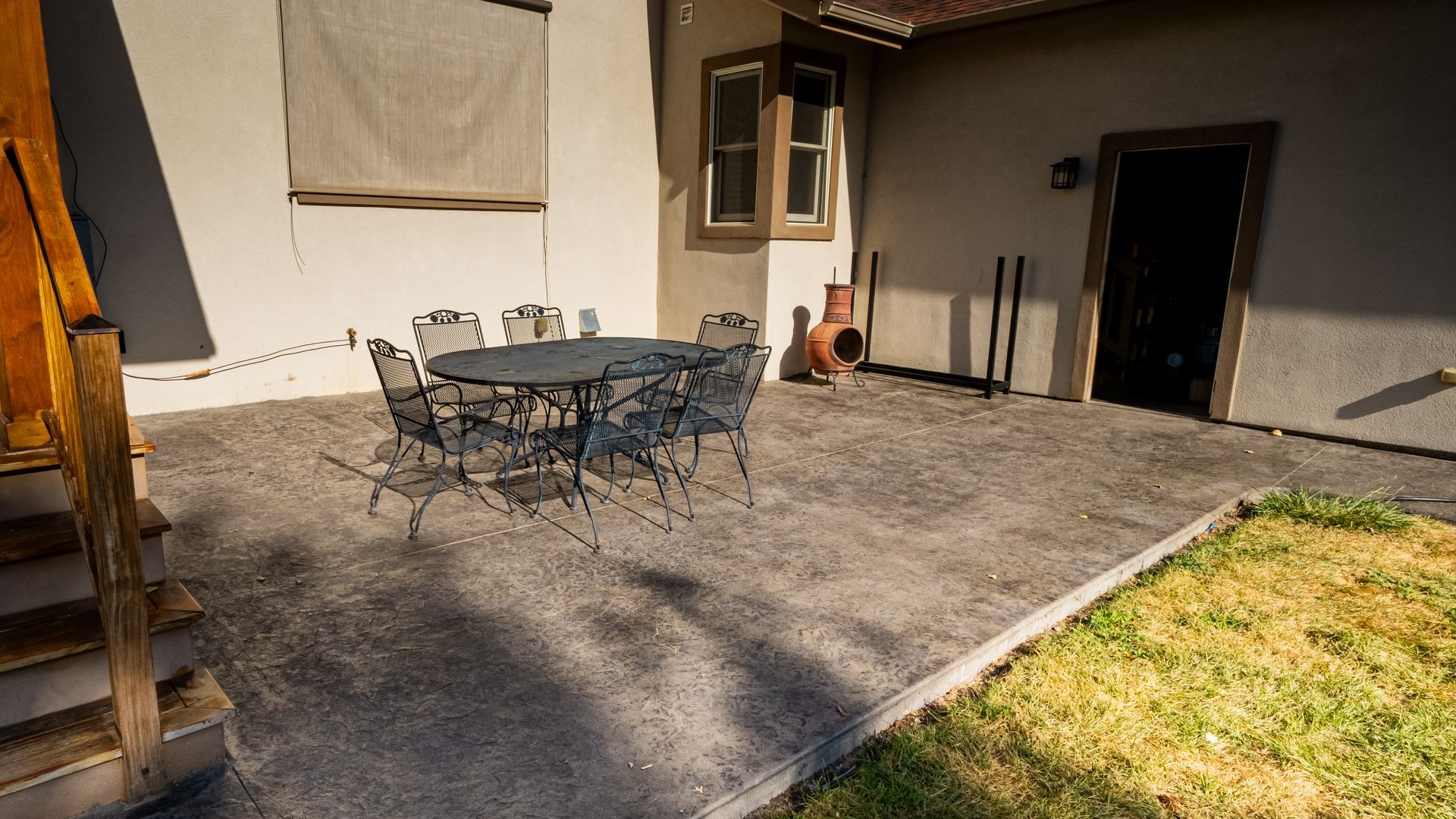 Patio with metal table and chairs on a concrete patio beside a house, with a patch of grass nearby.