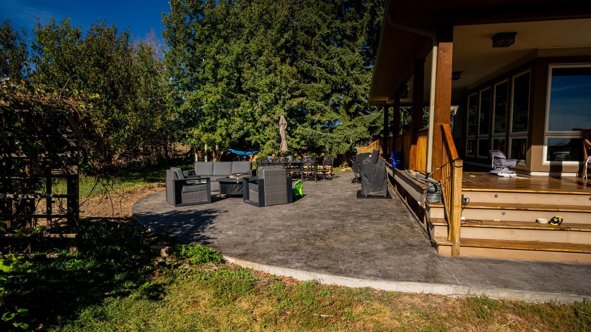 Backyard patio with black outdoor furniture, gravel ground, and a wooden porch beside a house