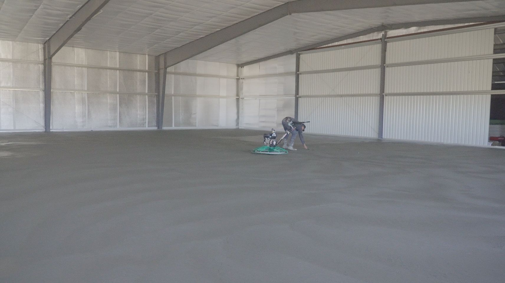 Interior of a large empty metal warehouse, with a person on a floor-cleaning machine near the center