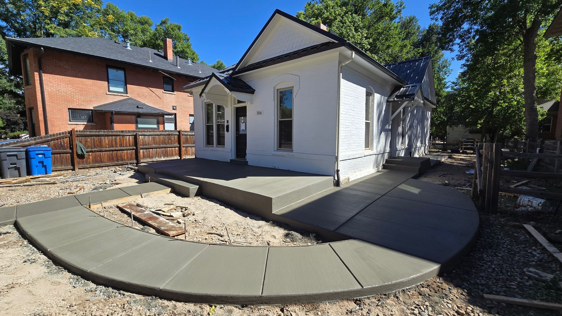 Small white house with a curved concrete patio and stone landscaping in a sunny backyard