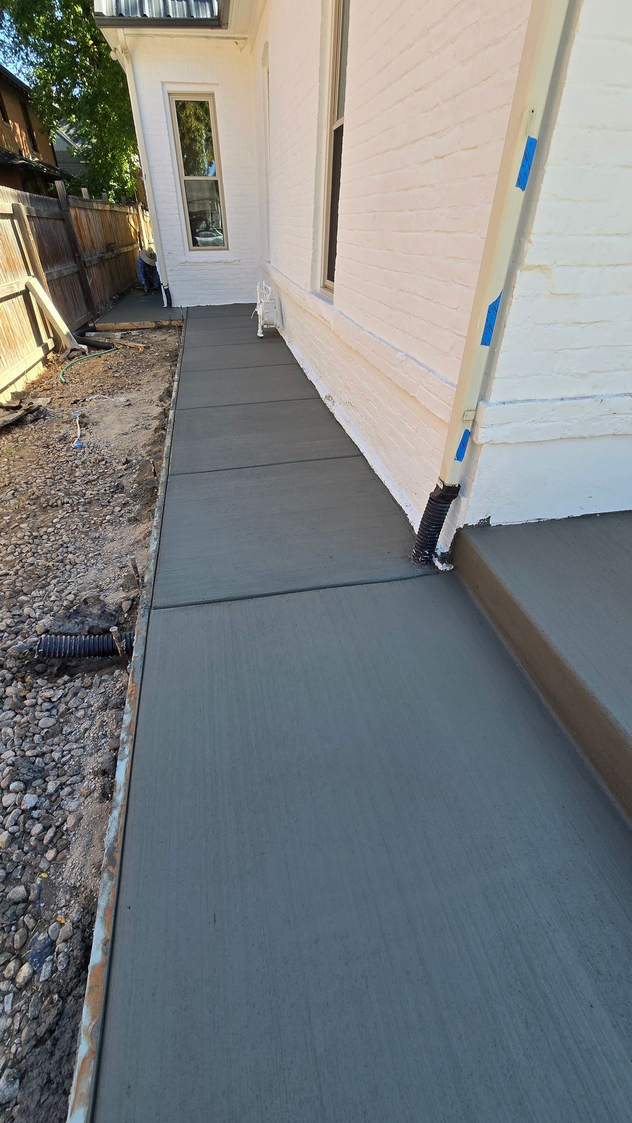 Concrete walkway beside a house, bordered by gravel and a blue-trimmed wall, leading to a door.