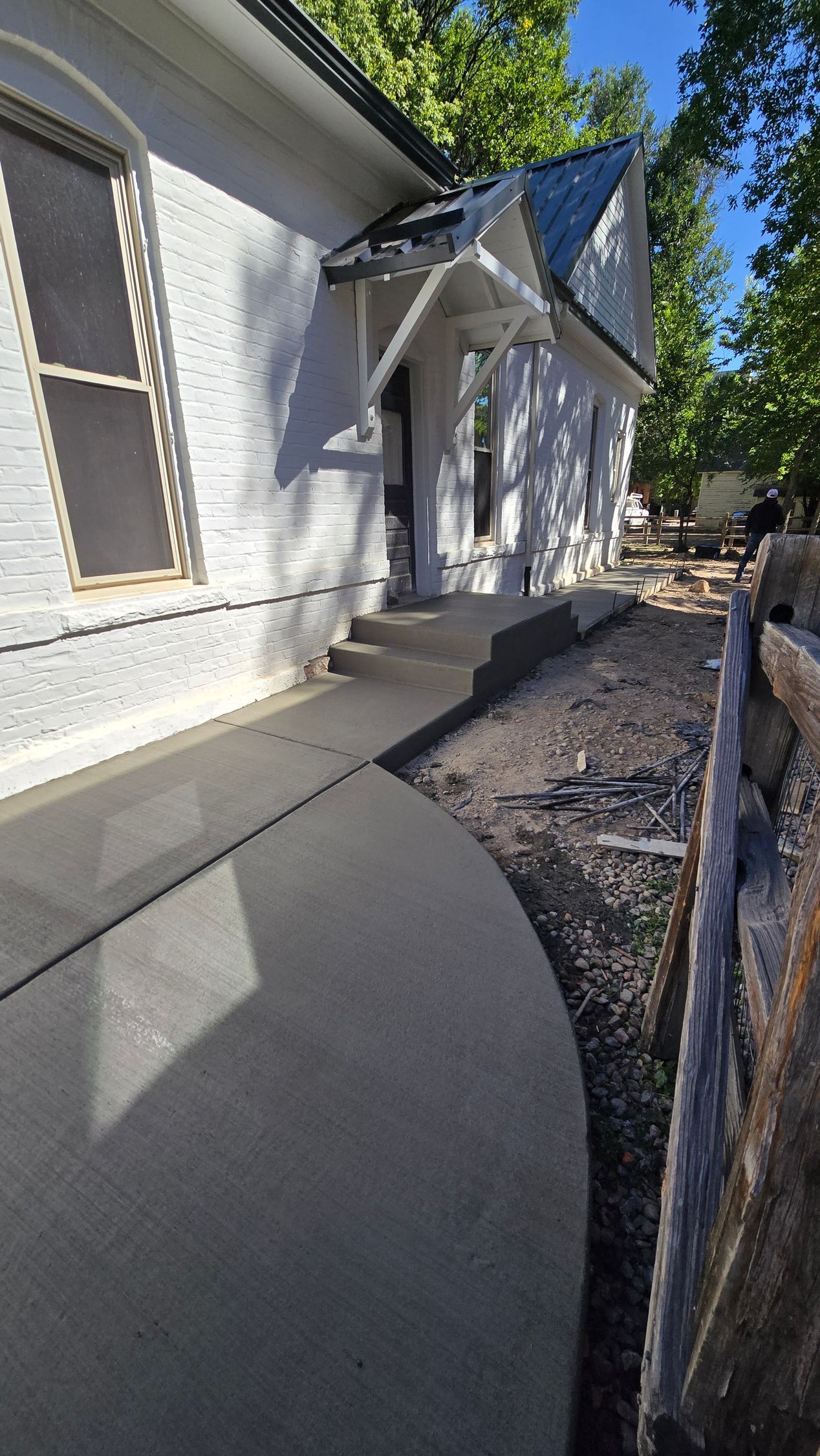White house side walkway with gray pavement, gravel strip, and a wooden fence in bright sunlight
