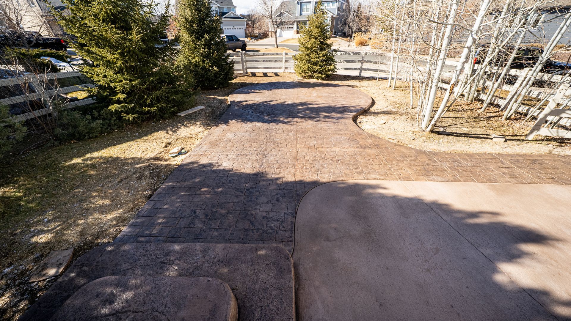 Rock-lined gravel path leading through a sunny landscaped yard with trees and shrubs