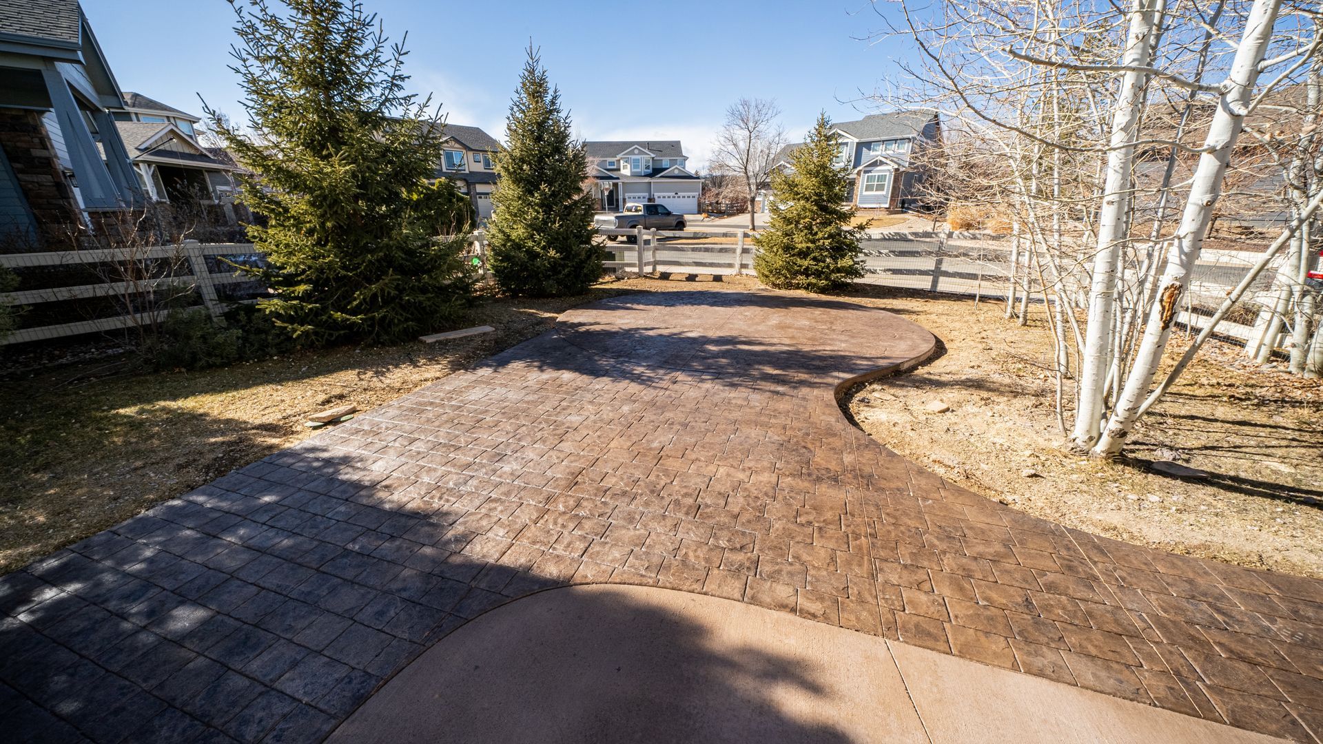 Curved brick walkway leading through a landscaped courtyard with evergreen trees and leafless birch trees.