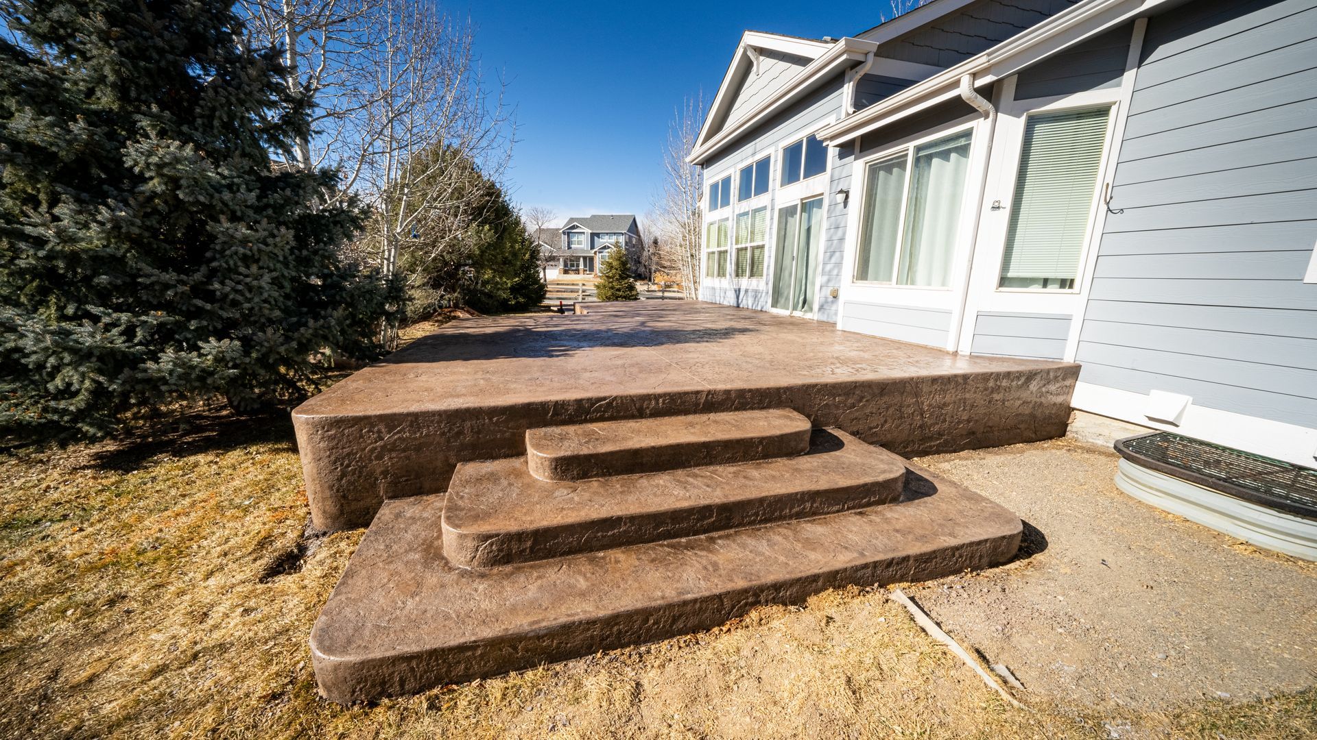 Front steps leading to a light blue house with large windows and a concrete patio in a yard