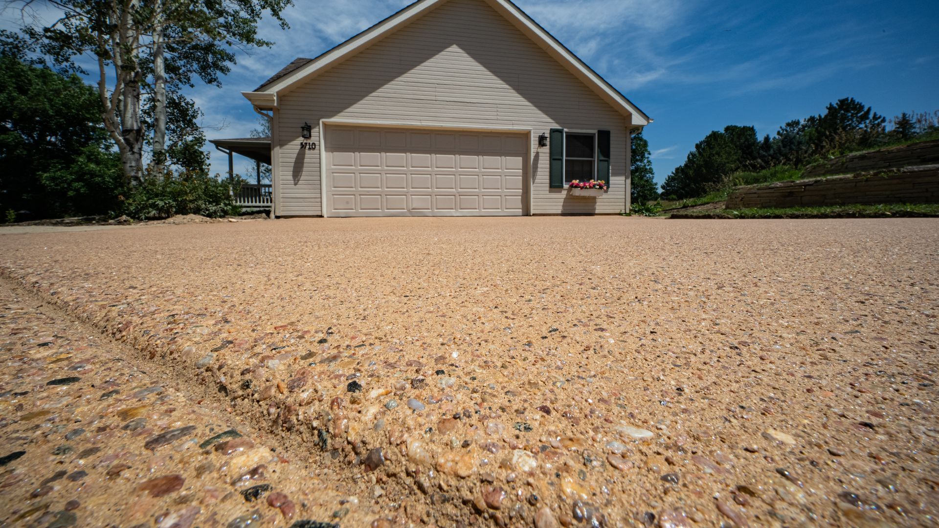 Single-story white house with a garage on a gravel driveway under a clear blue sky