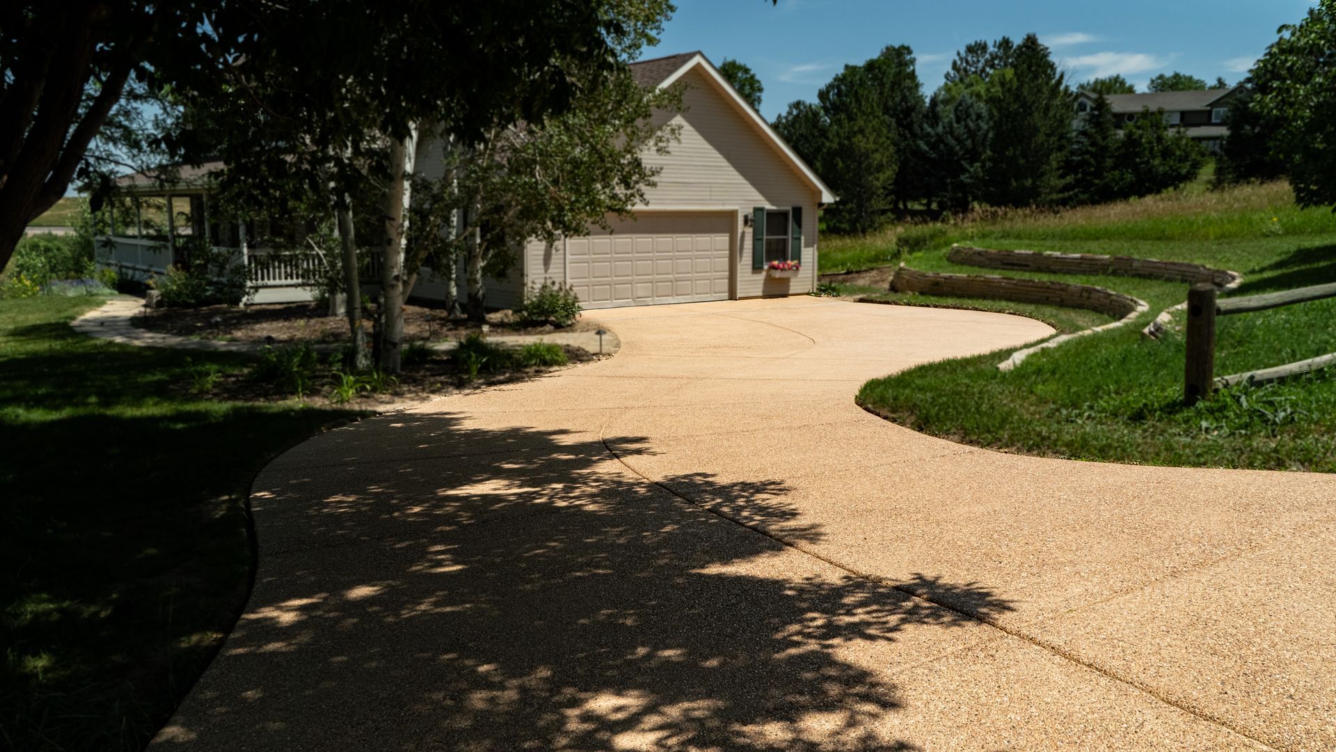 Curved gravel driveway leading to a house with trees and lawn, in bright sunlight.