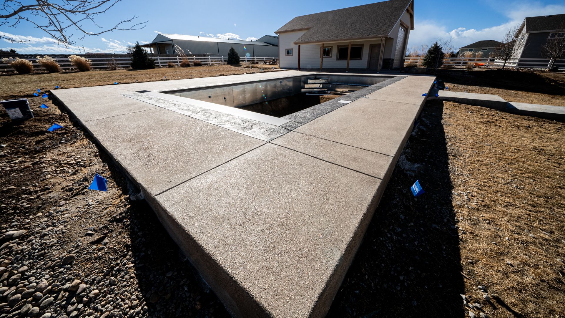 Concrete backyard patio with a sunken rectangular fire pit, surrounded by gravel and a house in the background