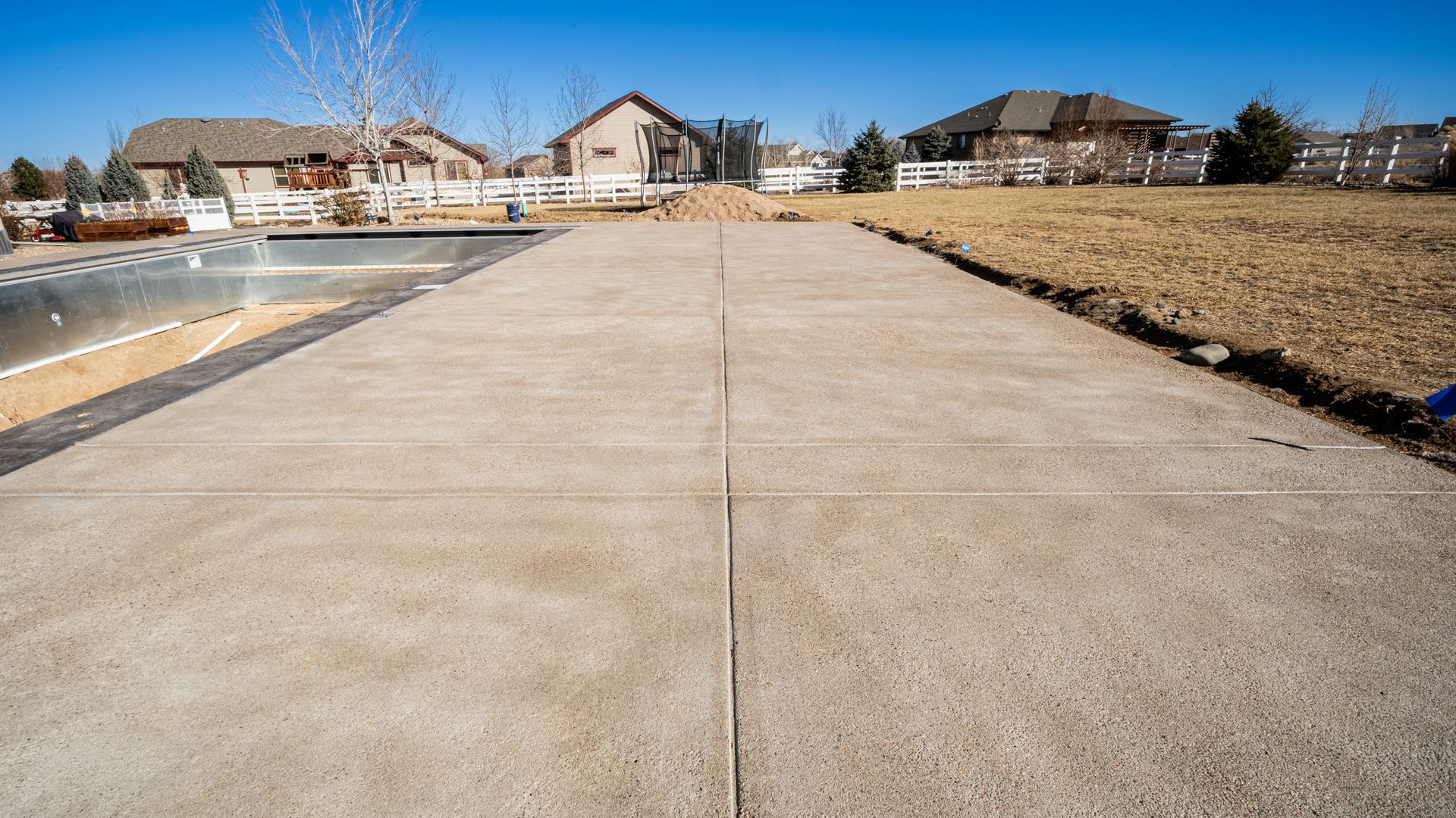 Wide concrete sidewalk beside a creek in a suburban neighborhood under a clear blue sky