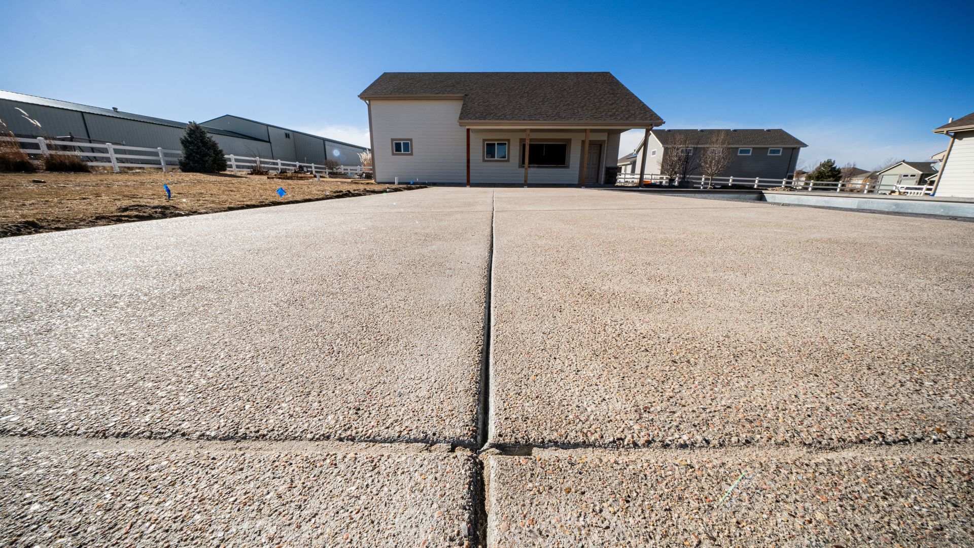 Concrete driveway leading to a small house under a clear blue sky, with open lots on either side