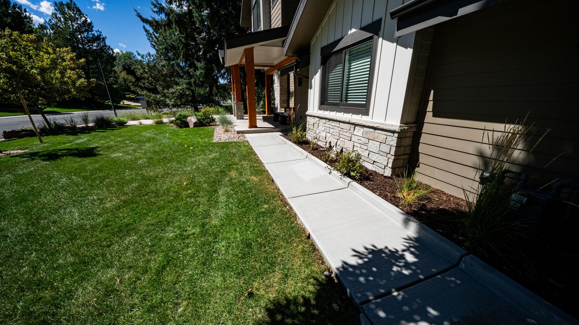 Front walkway beside a house with stone siding, green lawn, and trees in bright sunlight