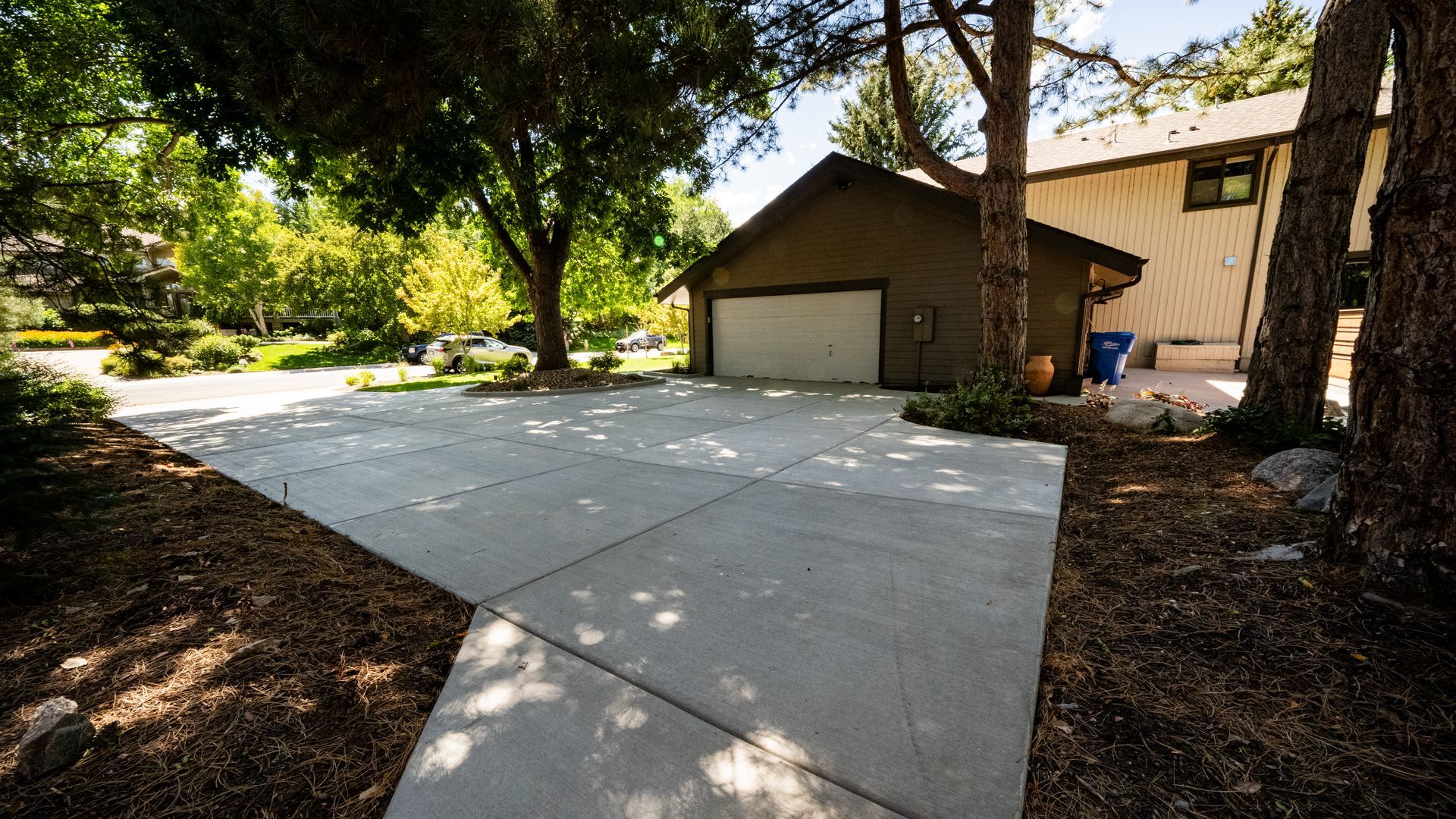 Concrete driveway leading to a tan garage under trees in a shaded suburban yard