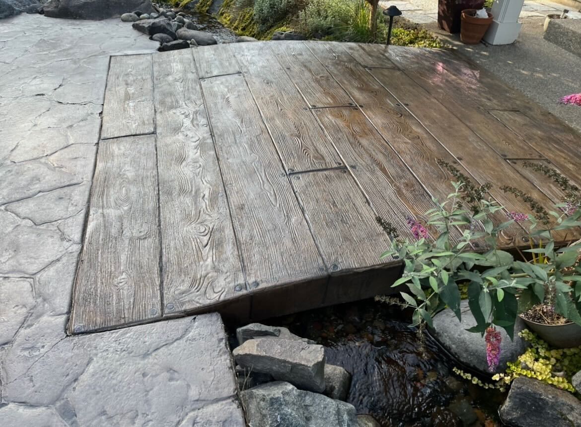 Temporary wooden bridge covering a broken sidewalk over a gap with rocks and plants nearby