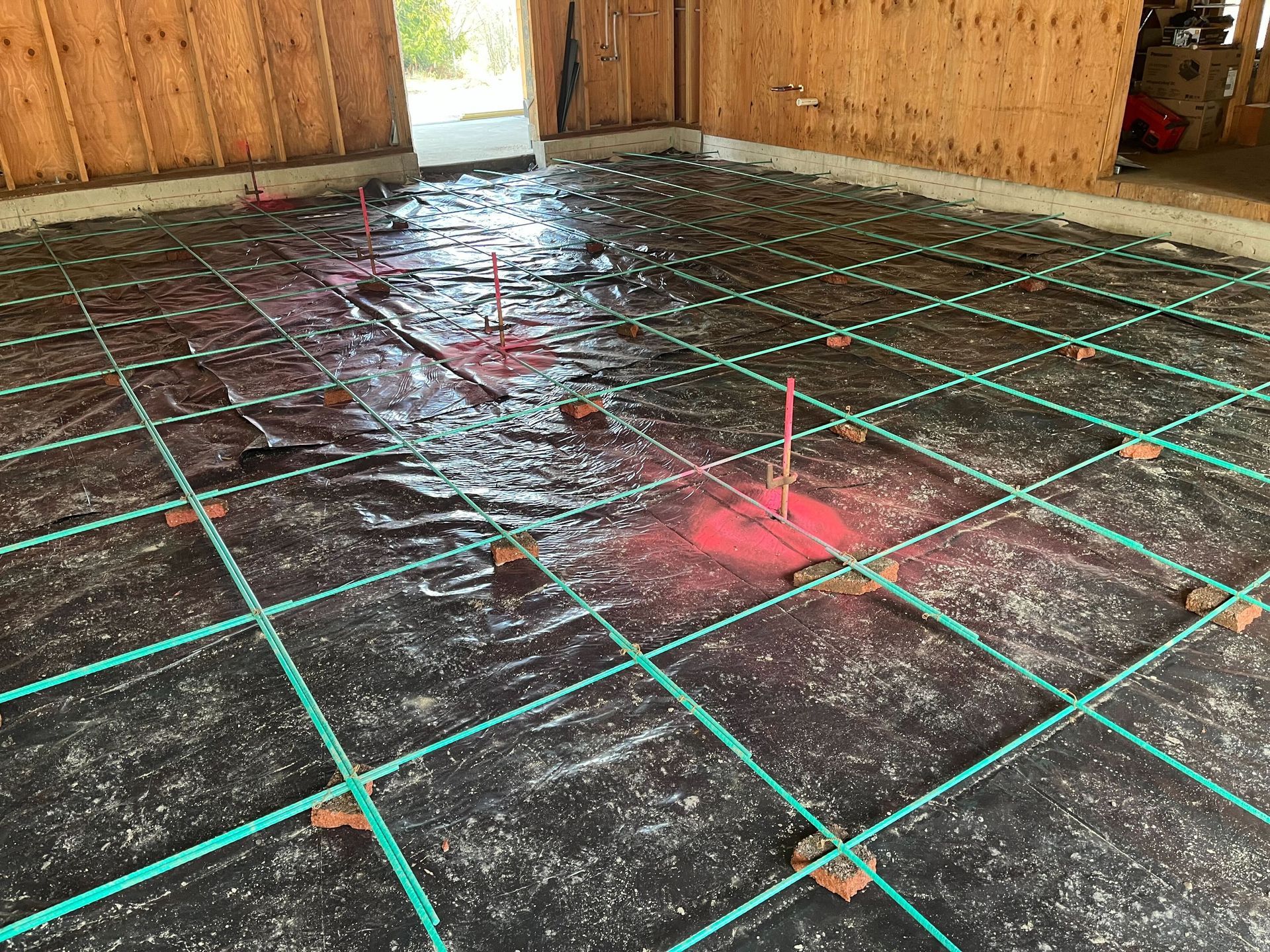 Wet concrete floor with green grid lines inside an unfinished wooden room