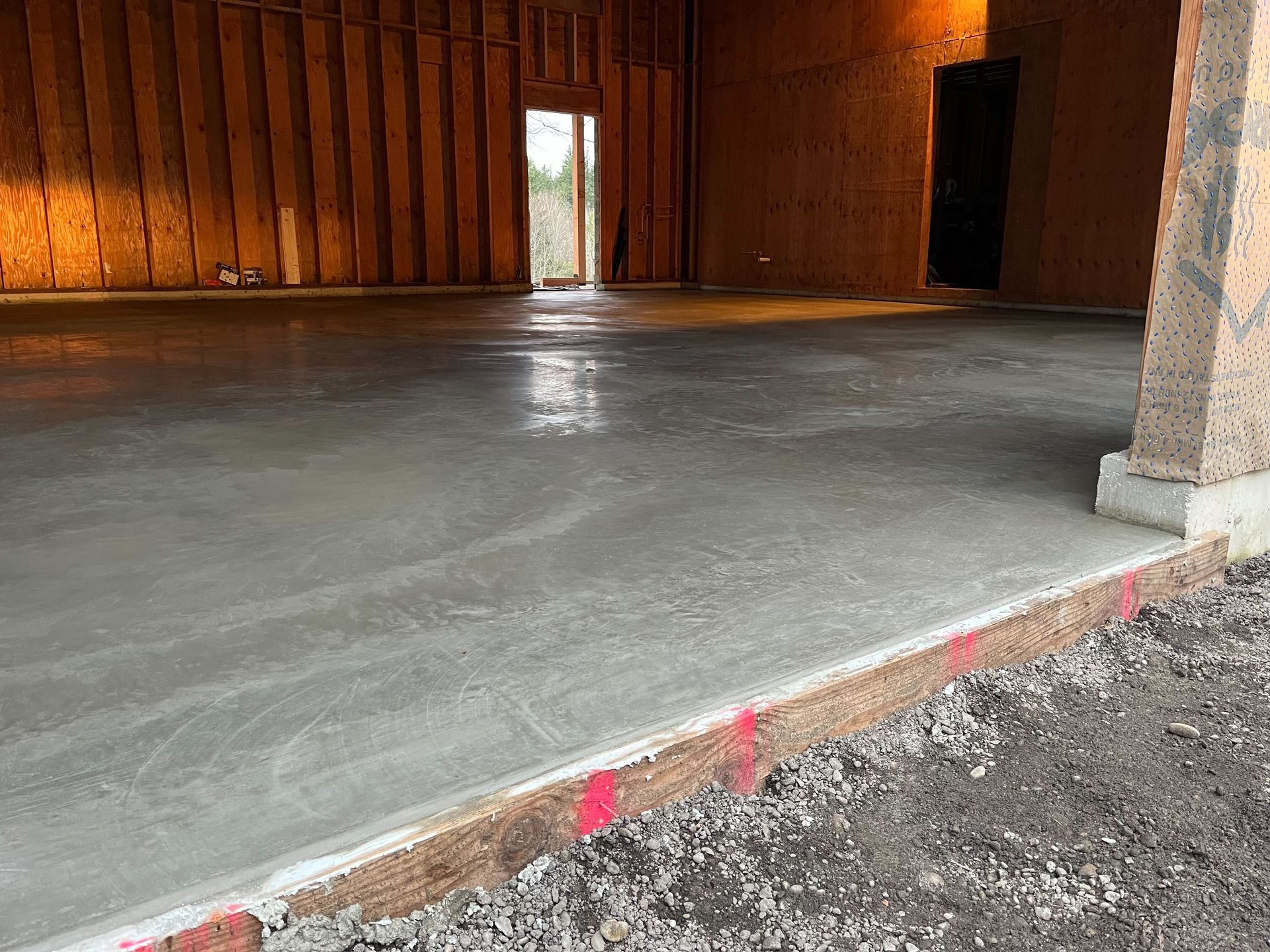 Empty wooden room with a newly poured concrete floor and a doorway at the far end