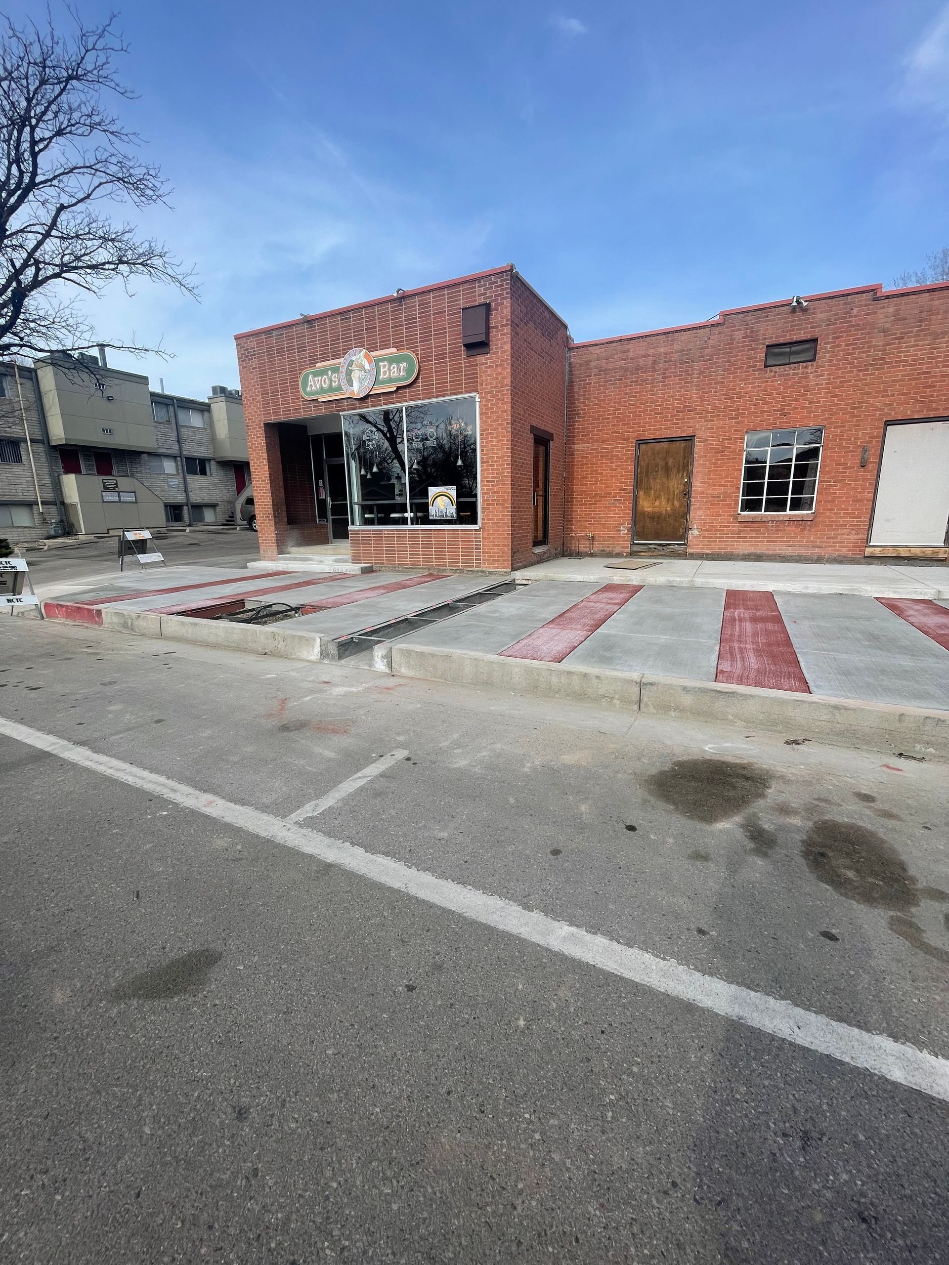 Brick storefront with striped accessibility ramp and sidewalk, viewed from the street on a sunny day