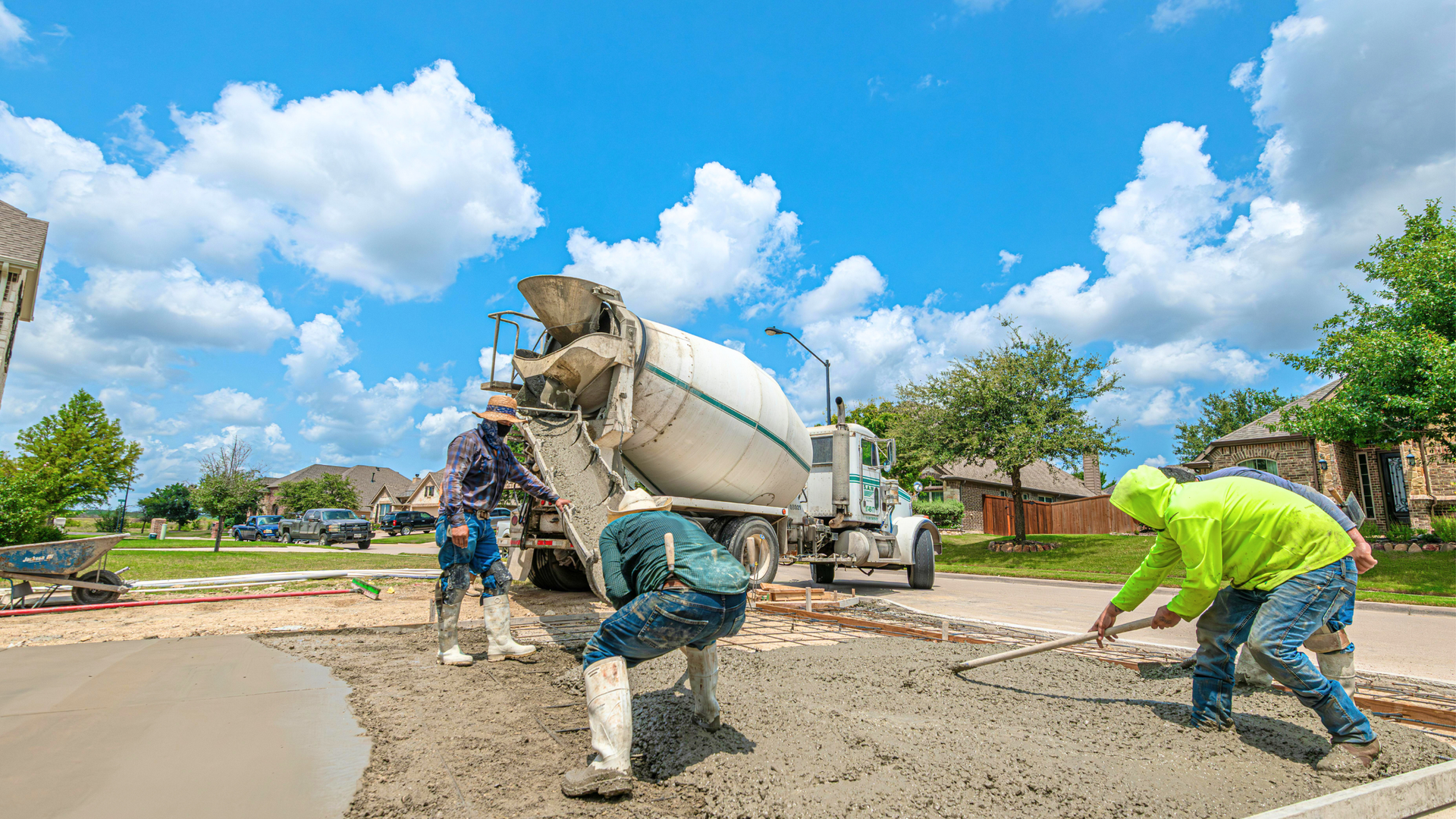 Construction workers pour concrete from a mixer on a sunny road under a blue sky.