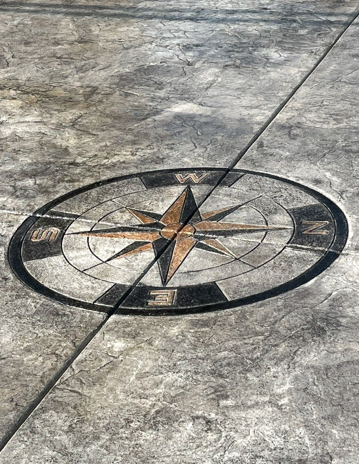 Compass rose mosaic embedded in a gray stone pavement with a diagonal crack line