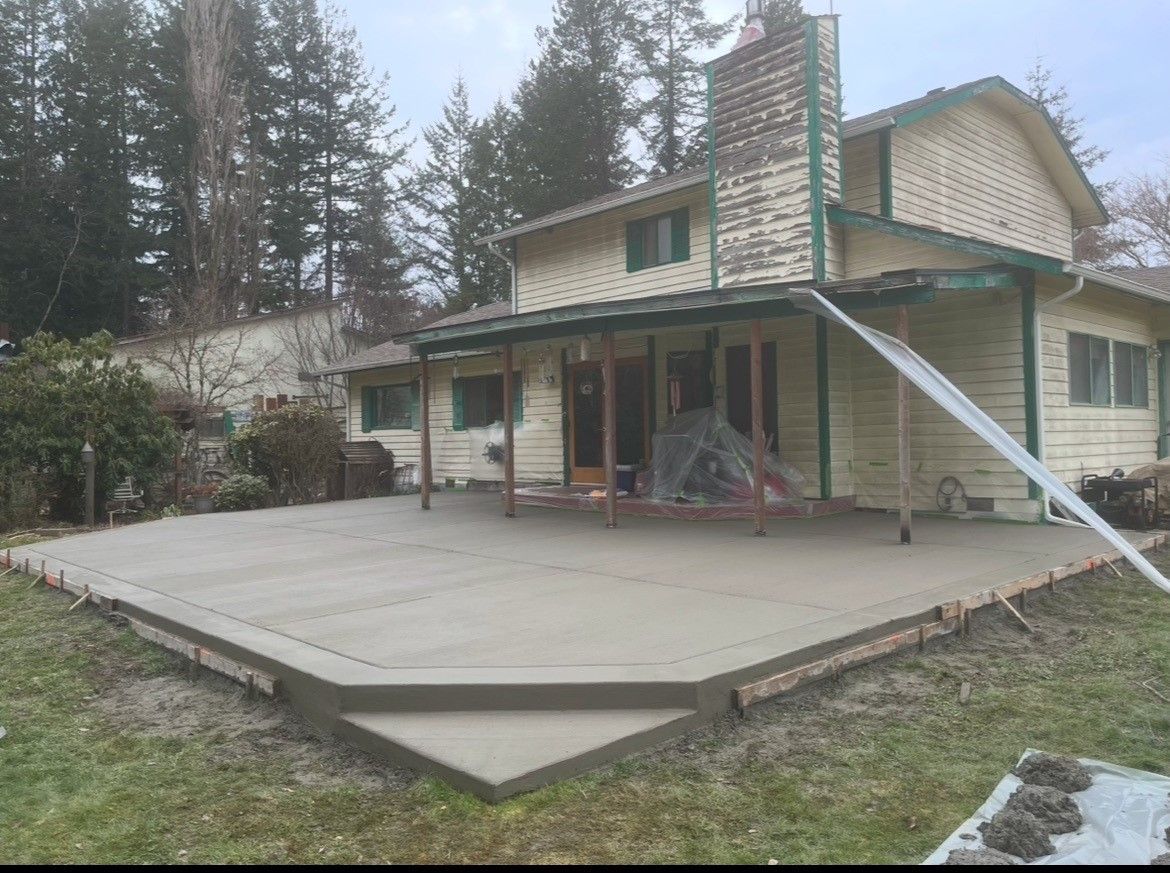 House with a large concrete patio and a slanted support beam in a wooded yard