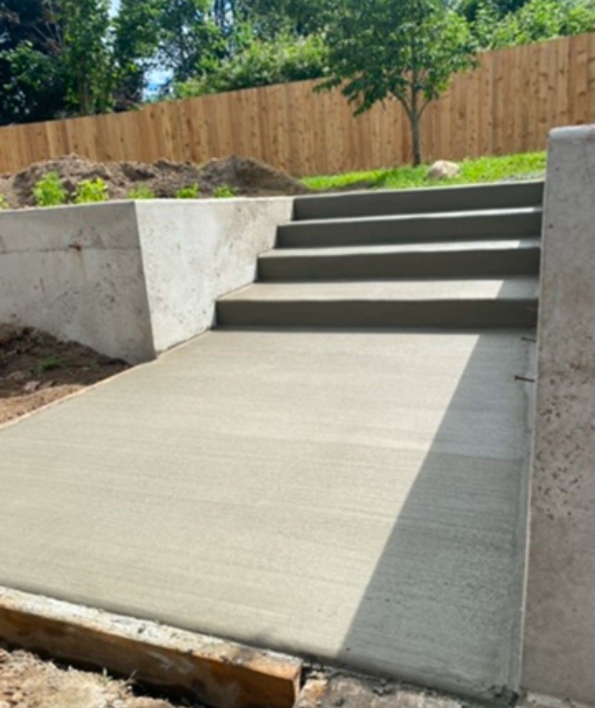 Concrete accessibility ramp and steps beside a wooden fence in a landscaped yard