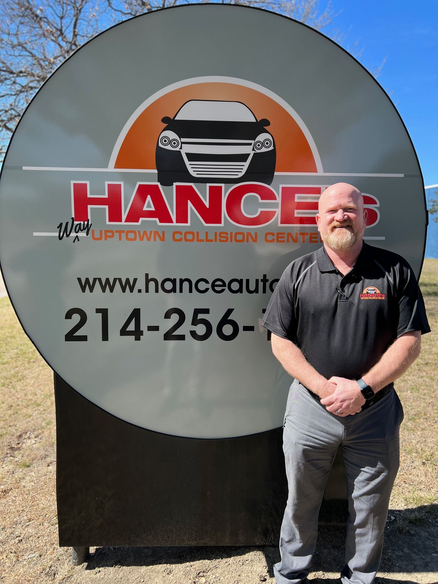 A man is standing in front of a sign that says hances uptown collision center.