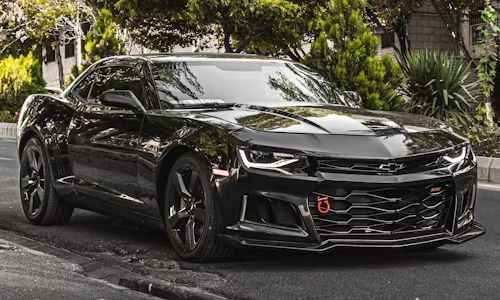 Black Chevrolet Camaro sports car parked on a road with trees in the background.